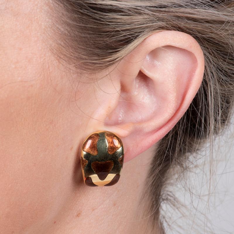 Aggiungi un tocco di estrosità al tuo abbigliamento con questi orecchini a cerchio in oro giallo 18 carati. Caratterizzati da un dettaglio smaltato a forma di astratto e da un fondello a omega, questi orecchini sono eleganti e comodi da indossare.
