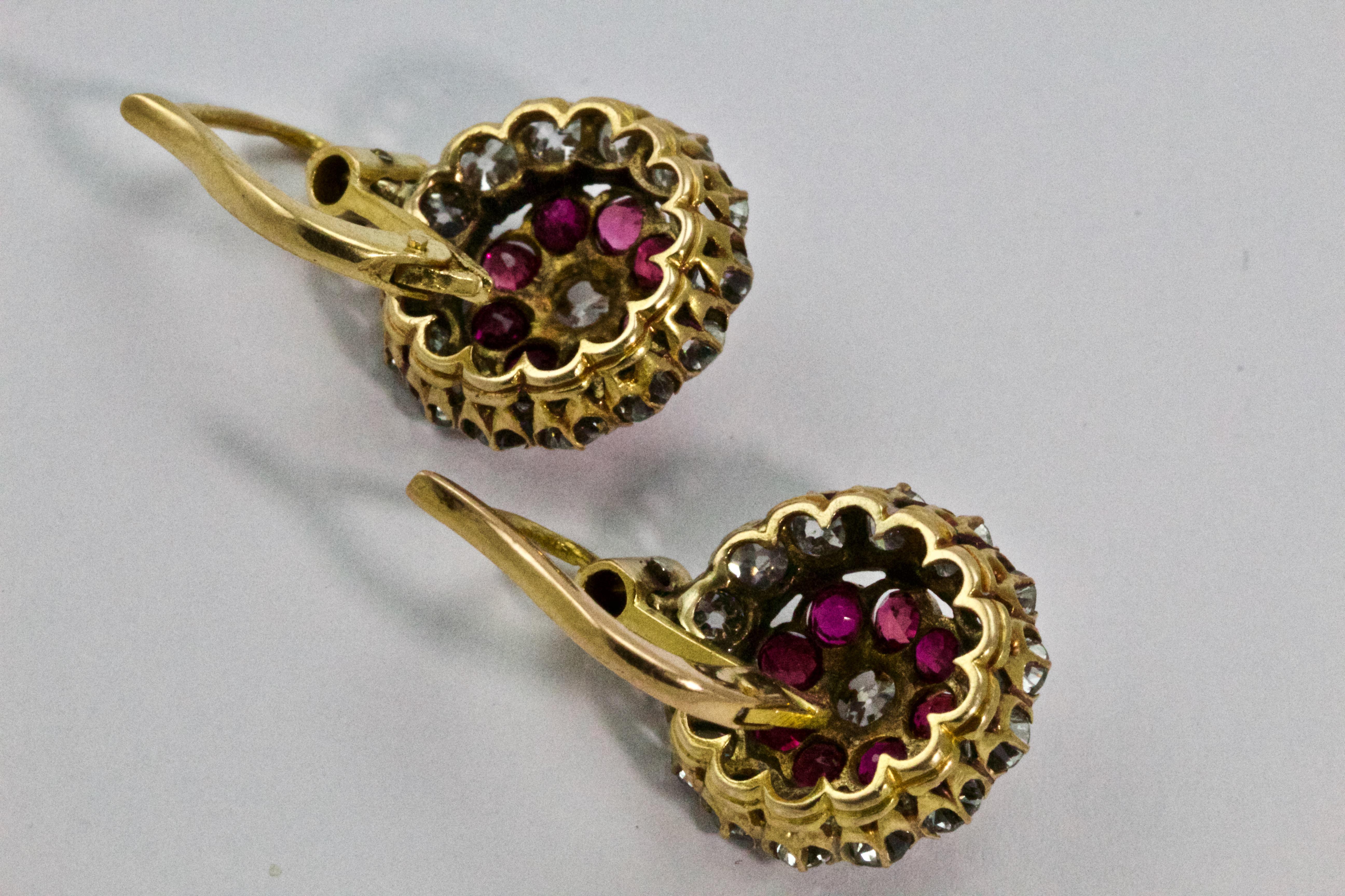 This magnificent pair of earrings are circa 1900 and modelled in 18 karat gold throughout. The central old European cut diamonds are claw set surrounded by a delightful halo of natural rubies and a further halo of diamonds. Each drop is suspended