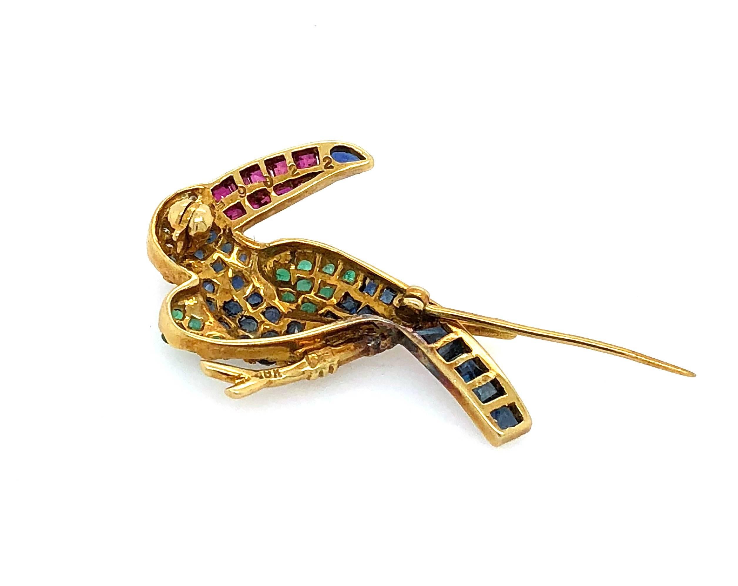 This beautiful brooch features a Toucan bird with multi-colour stones in 18K yellow gold setting. The beak is made of 10 Rubies of 0.32 carats with 5 Round Brilliant diamonds and a Sapphire around the face. There are 13 natural emeralds of 0.26