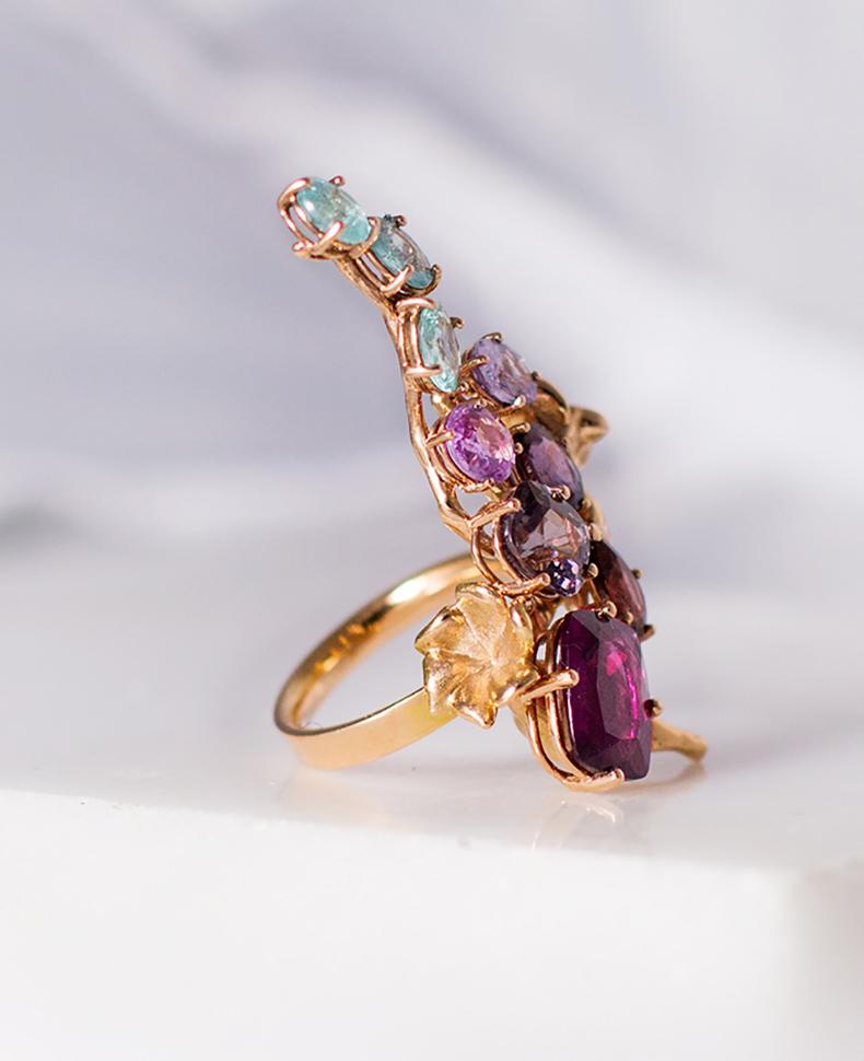 An unusual form makes this 18 karat rose gold contemporary cocktail cluster ring an art object. It is encrusted with: sapphires, Paraiba tourmalines, spinel and garnet rhodolite, 11 carats in total. 

The work is accurate and the piece sparkles as