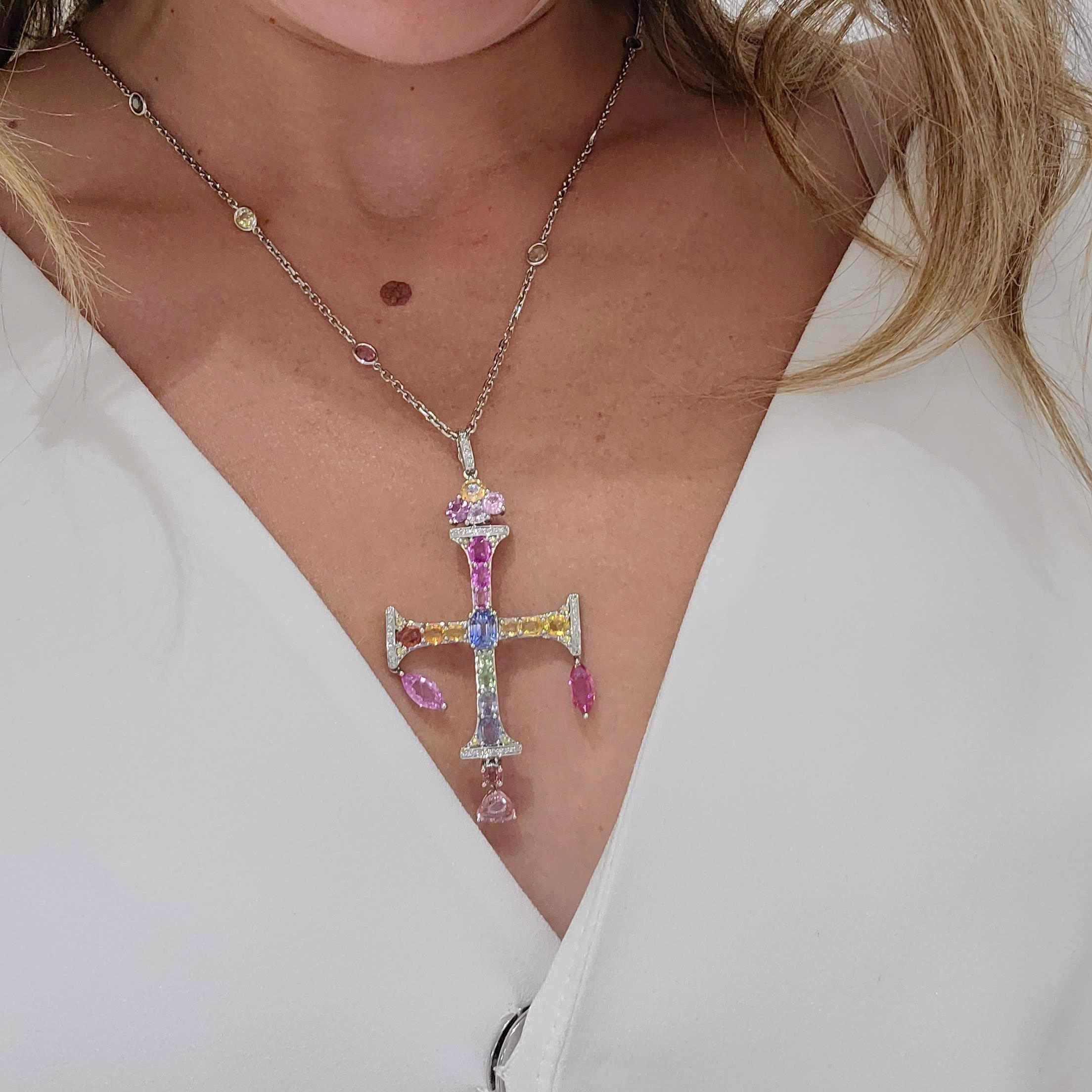 This beautiful 18 karat white gold cross is set with Round Sapphires in shades of blue, yellow, pink, orange and green. Pink Sapphires in Marquis and Trillion cut dangle from the ends which have been set with Diamonds. The cross and it's Diamond