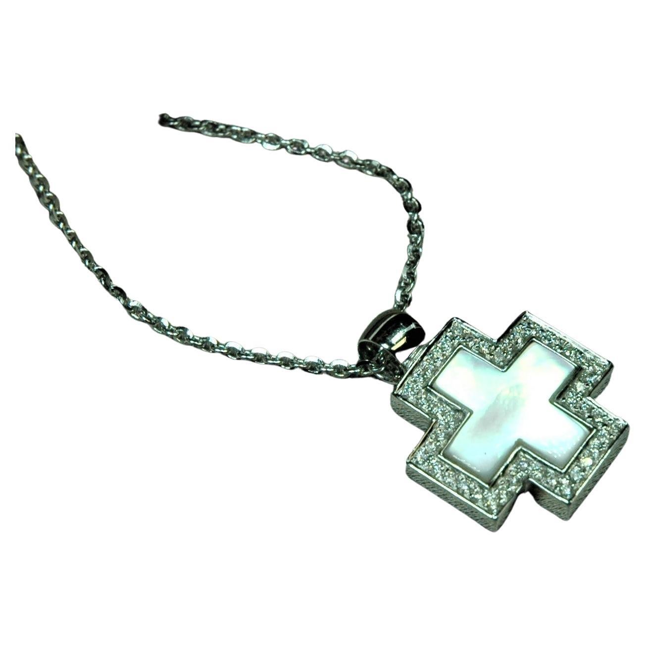Square-shaped cross in white gold 18 kt., embellished in the center by a cross in white mother-of-pearl and surrounded by brilliant cut diamonds (0.40 ct). The chain is a diamond groumette. The counter-link of the pendant is fixed and rounded,
