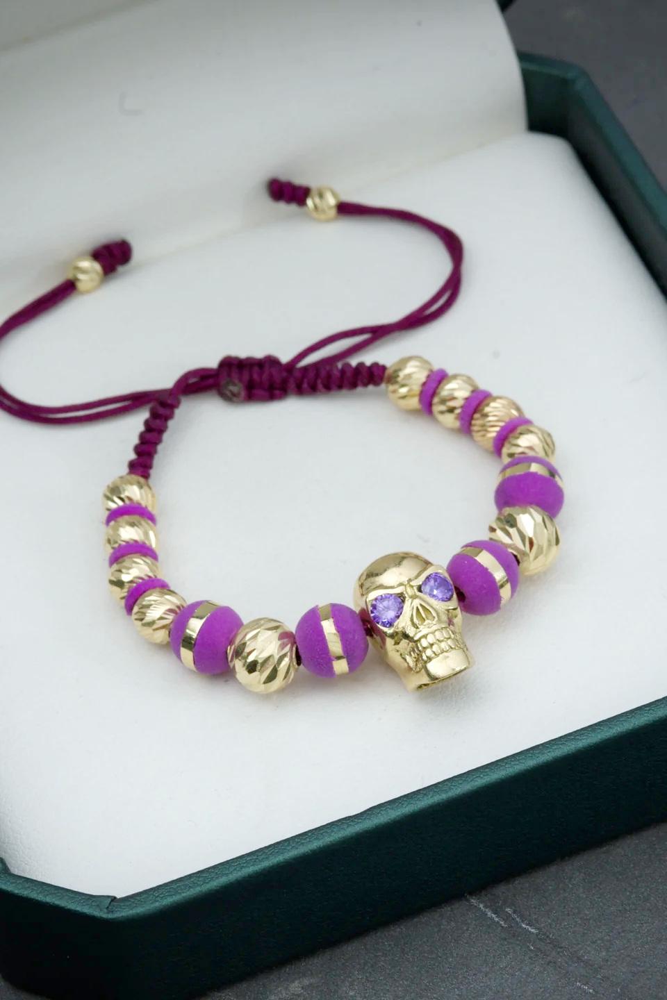 Bracciale in oro giallo 18 carati con un grande teschio centrale incrostato di cristalli Swarovski viola, 4 sfere di neoro e 12 ulteriori sfere sfaccettate di varie dimensioni, montato su filo viola regolabile

Peso totale del bracciale: 11.15