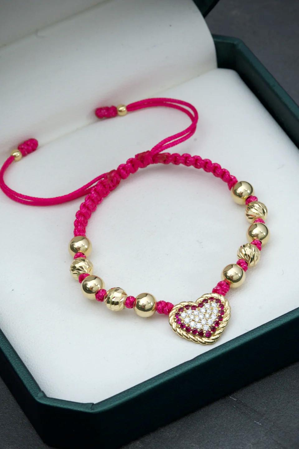 Bracelet en or jaune 18 carats avec un cœur central incrusté de cristaux Swarovski clairs et fuchsia, 8 boules lisses et 4 boules facettées de différentes tailles, monté sur un fil fuchsia réglable.

Poids total du bracelet : 4,35 grammes
Poids du