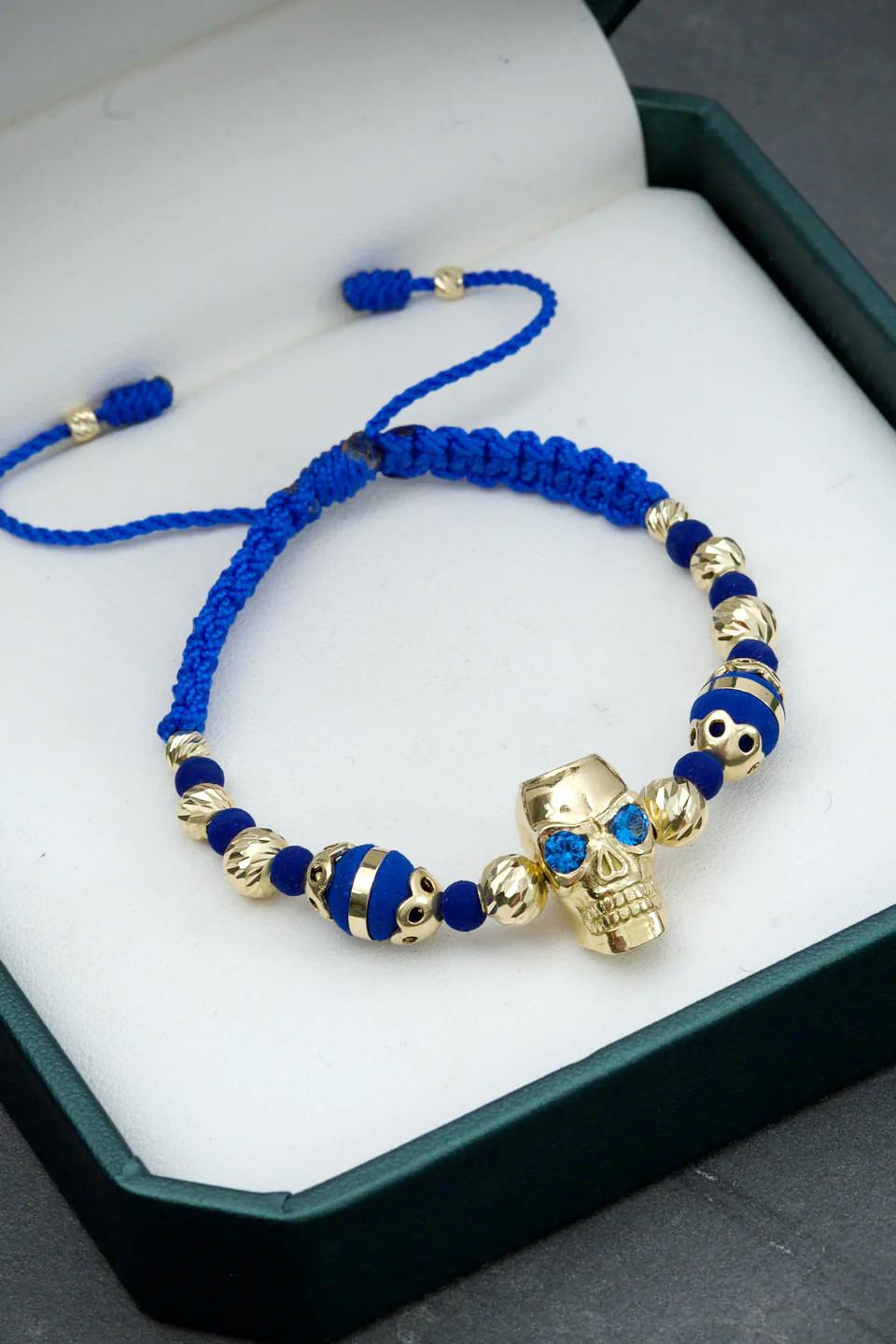 Bracciale in oro giallo 18 carati con un grande teschio centrale incrostato di cristalli Swarovski blu, 2 sfere a canestro e 10 ulteriori sfere sfaccettate di varie dimensioni, montato su filo blu regolabile

Peso totale del bracciale: 10,8