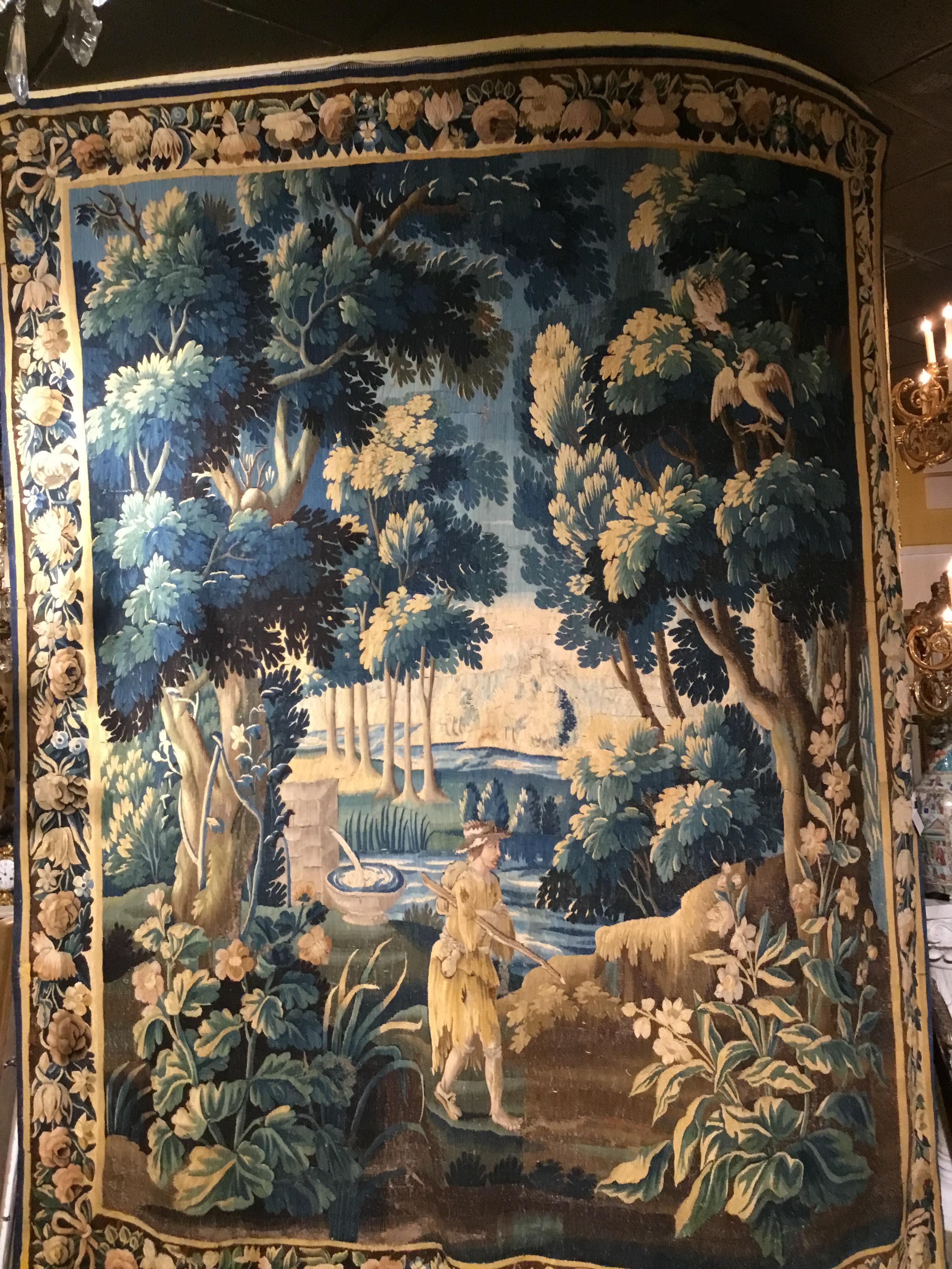 Green, gold, brown and tan hues are used in this large tapestry. Forest in lovely shades of
Greens and blues with birds in the upper right corner and a hiking man with a fountain
In the lower portion of this work. It is very old, handwoven without