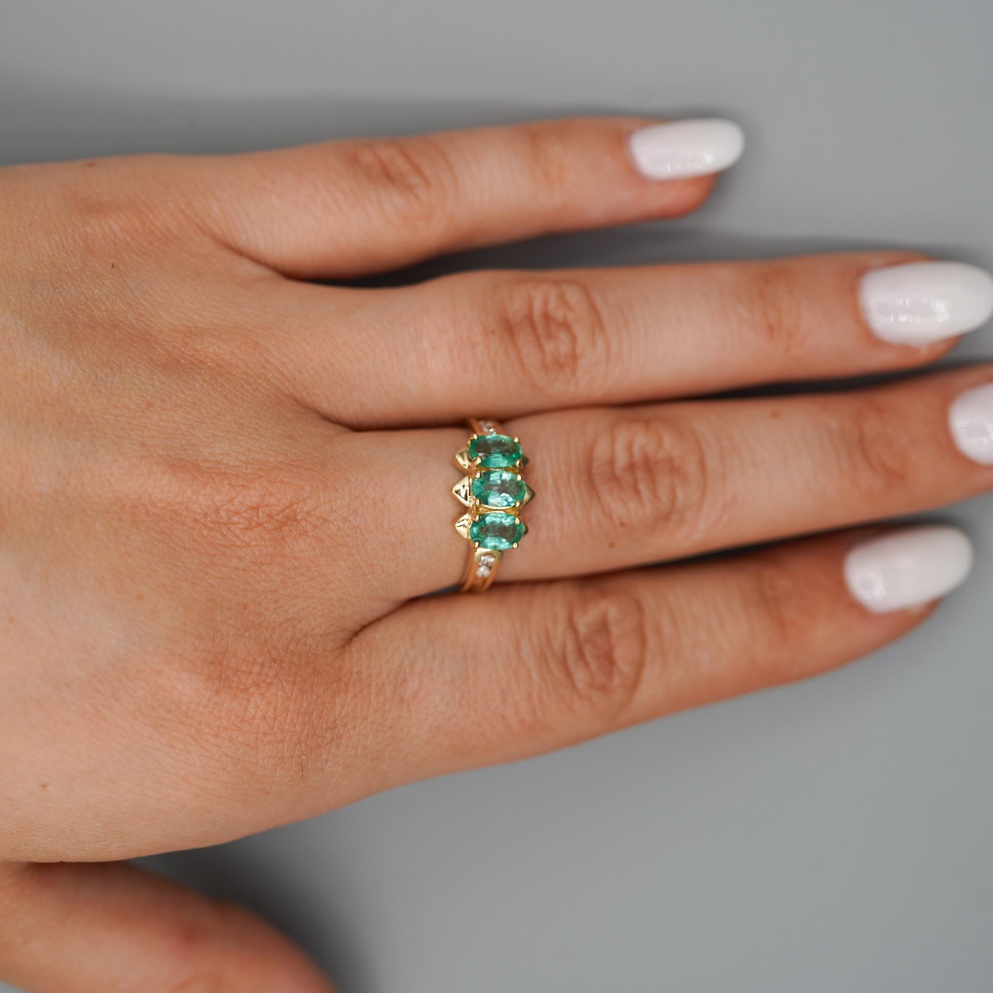 This 14K yellow gold three-stone ring features 1.80 carats of oval-cut emeralds accented by four round diamonds for added brilliance. The vivid pastel green stones are set in a sharp, polished frame that highlights their natural character and