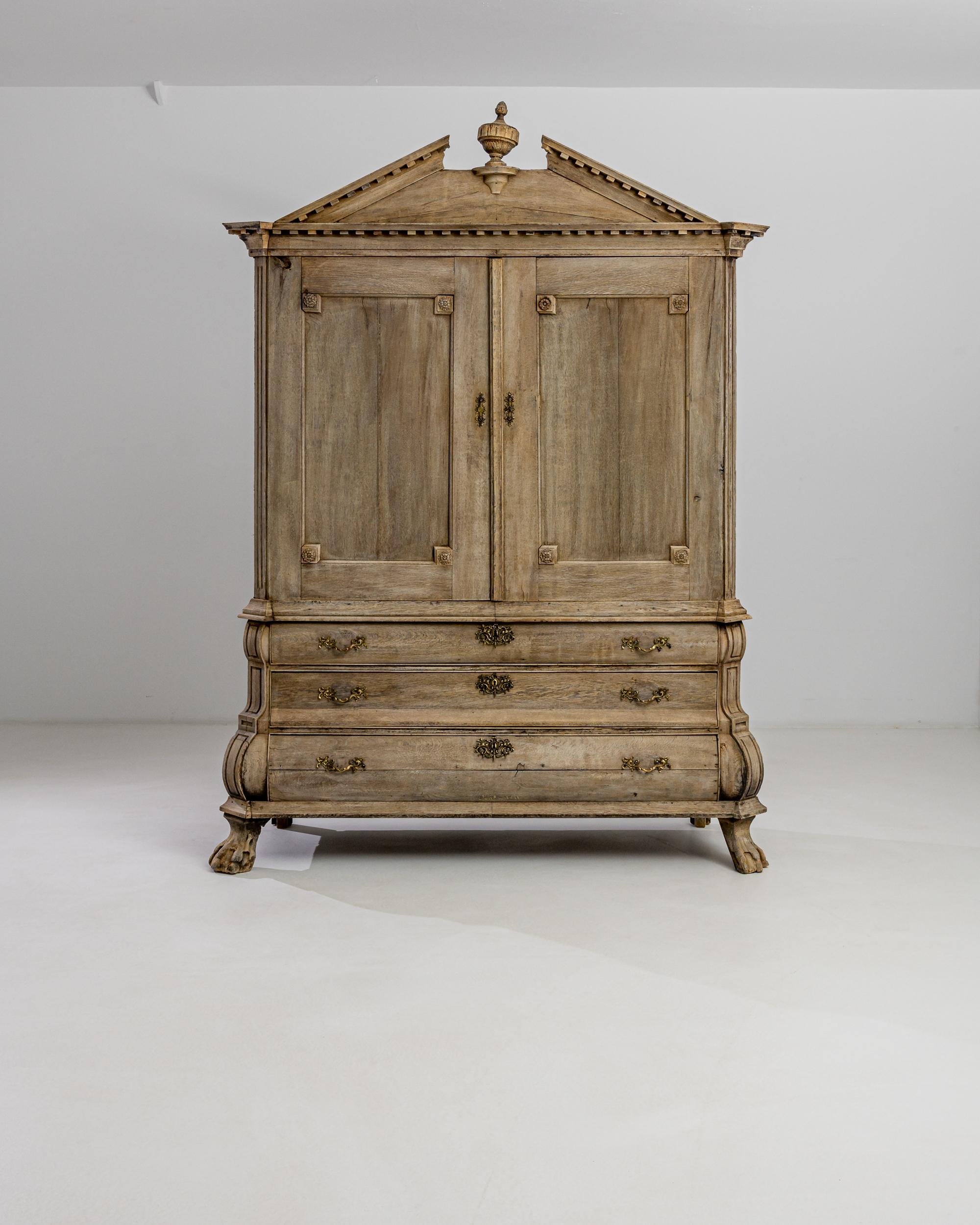 Hand-crafted in the Netherlands circa 1800, this impressive chest boasts an elaborate pediment with a carved cup crowing its top; an ample square-paneled torso and a bombe chest of drawers raised on claw feet. The eclectic combination of
