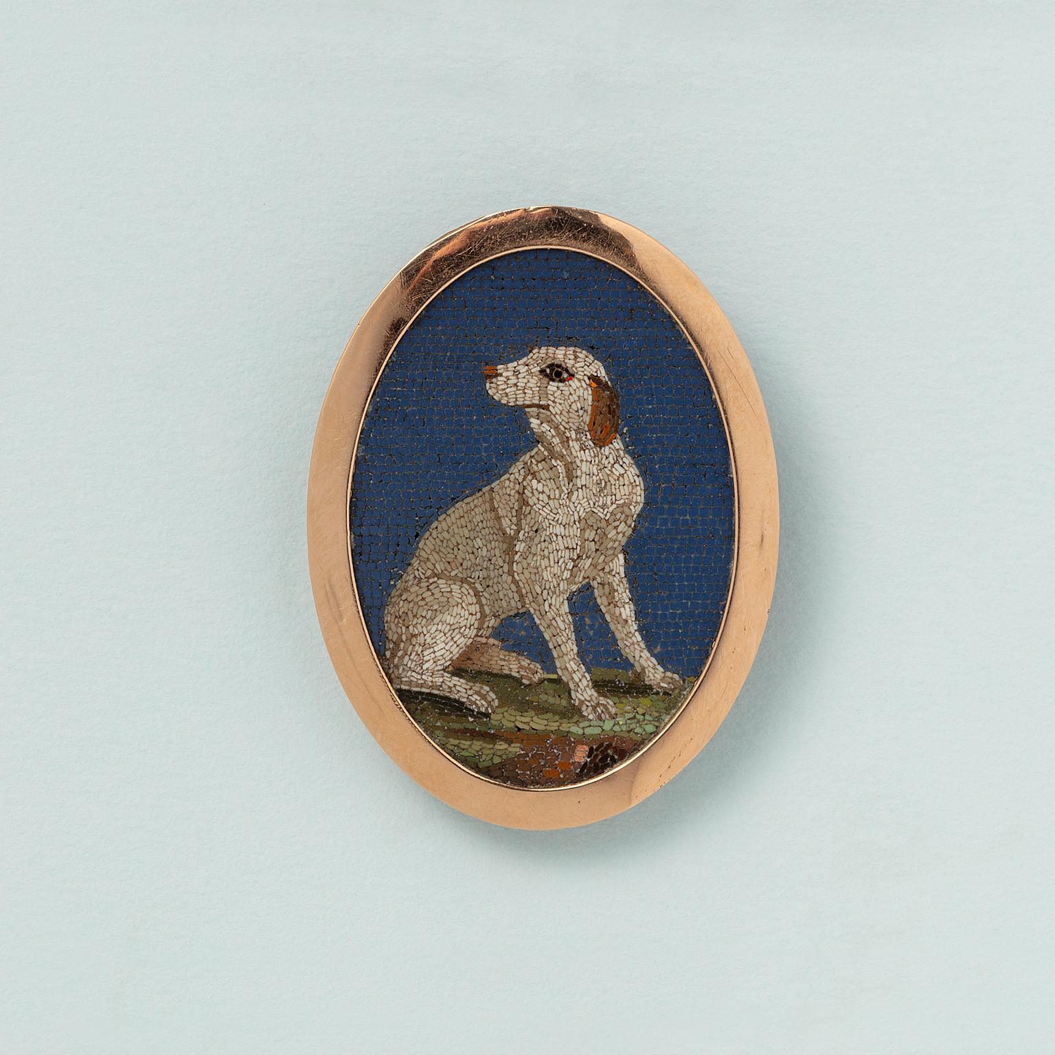 An oval micro mosaic of a dog with a blue background in an 18 carat gold border, with a silver setting which can be either a brooch or a stand, Rome, circa 1800.

weight: 9.4 g
dimensions with border: 4.5 x 3 cm
dimensions micro mosaic: 4 x 2.7 cm
