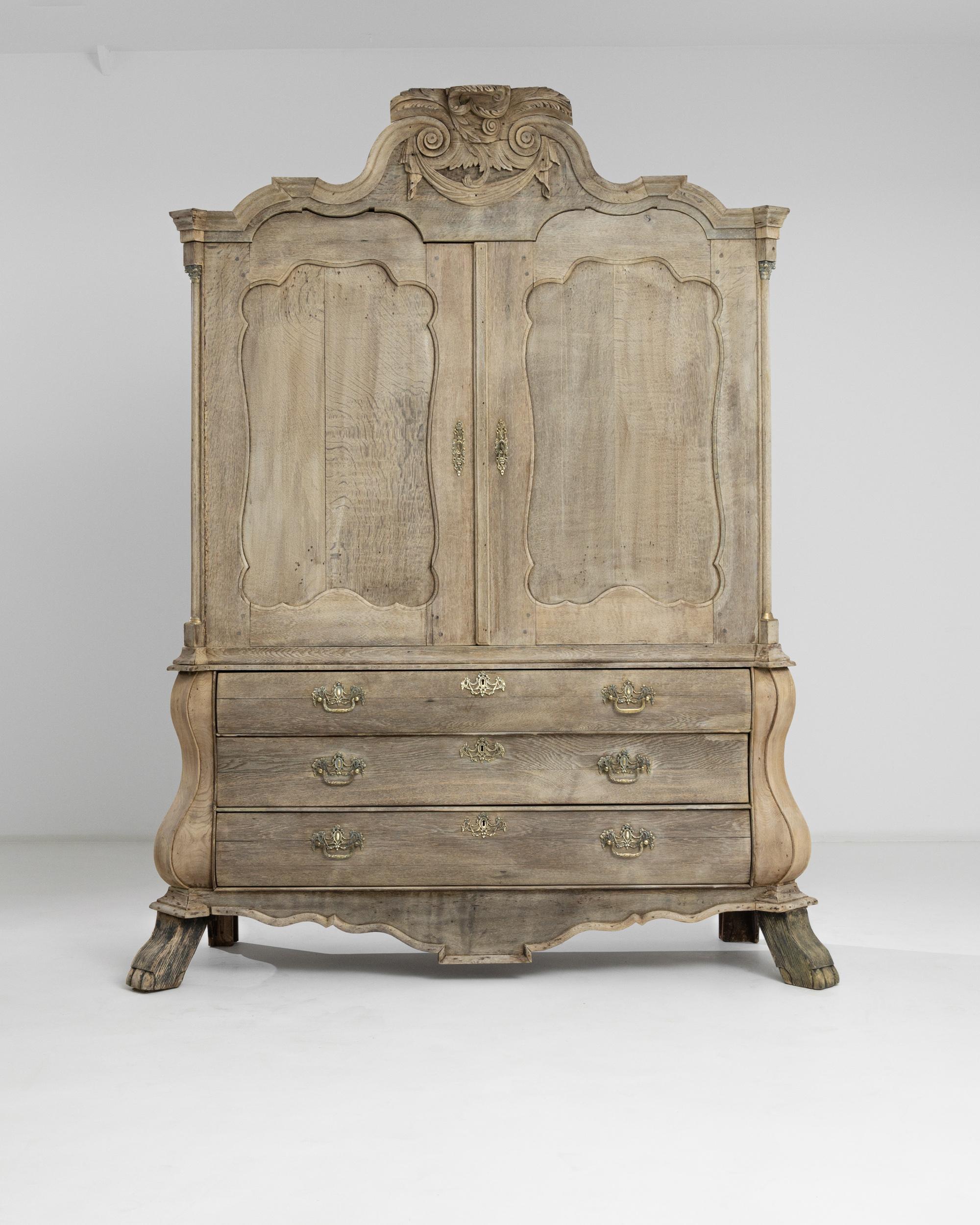 A rare antique cabinet produced in the Netherlands, circa 1800. An imposing carved chest stands on squared hoof feet, betraying a French influence. Flanked by discreet columns, the carved front doors are crowned by an ornate top with a lush central