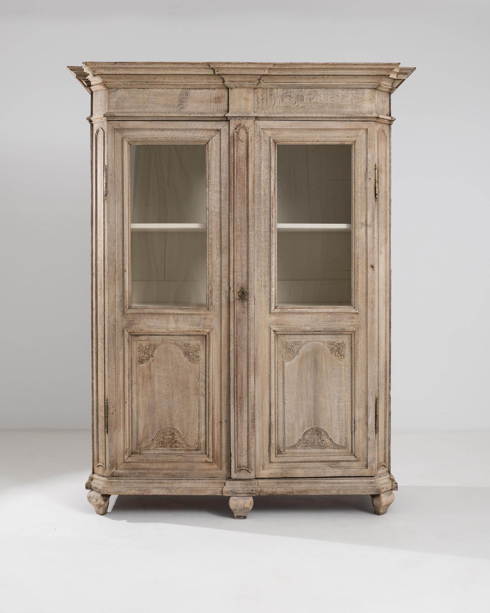 This antique oak vitrine possesses a springtime freshness. Built in Belgium circa 1800, the faceted form of the cabinet creates an impression of delicacy despite its ample size. A magnificent tiered cornice adds a crowning detail, while at the base