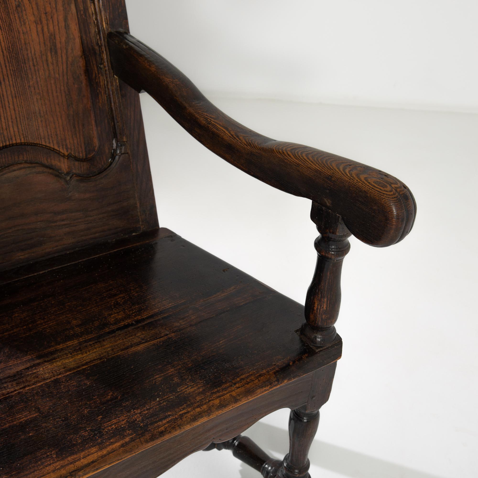 A wooden armchair with original patina from the United Kingdom, produced circa 1800. A regal armchair constructed with a gorgeous dark oak, featuring a gently angled back, a capital “I” shaped stretcher, and an apron under the seat. The strict lines
