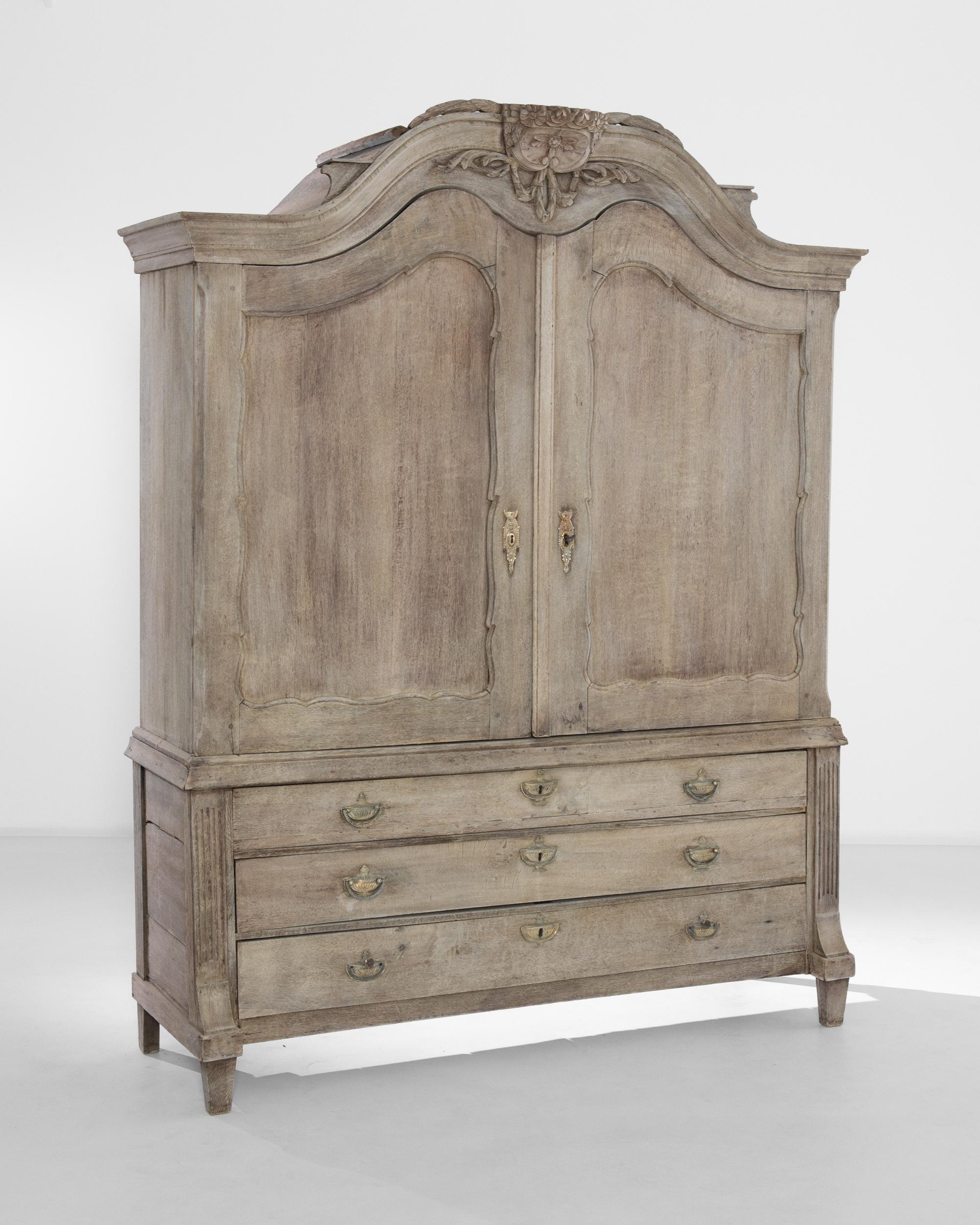 A bleached oak cabinet from The Netherlands, produced circa 1800. A massive wooden chest standing nearly seven feet tall, featuring an arched, locking double door cabinet of three shelves, and three sliding drawers with brass escutcheons and hanging