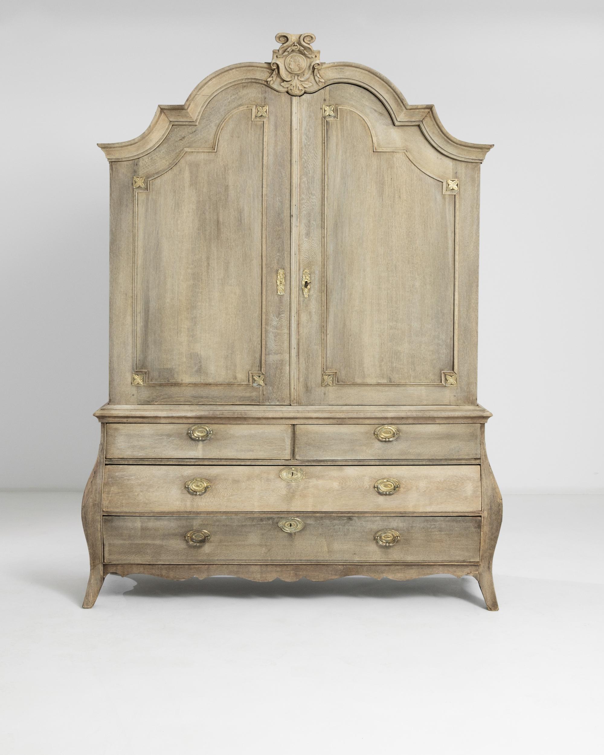 A large Dutch bleached oak cabinet. Seemingly untouched by time, this well preserved cabinet offers ample storage space across numerous shelves and drawers. Stamped metal keyhole and drawer handle ornaments, in addition to a Roman figurehead carved