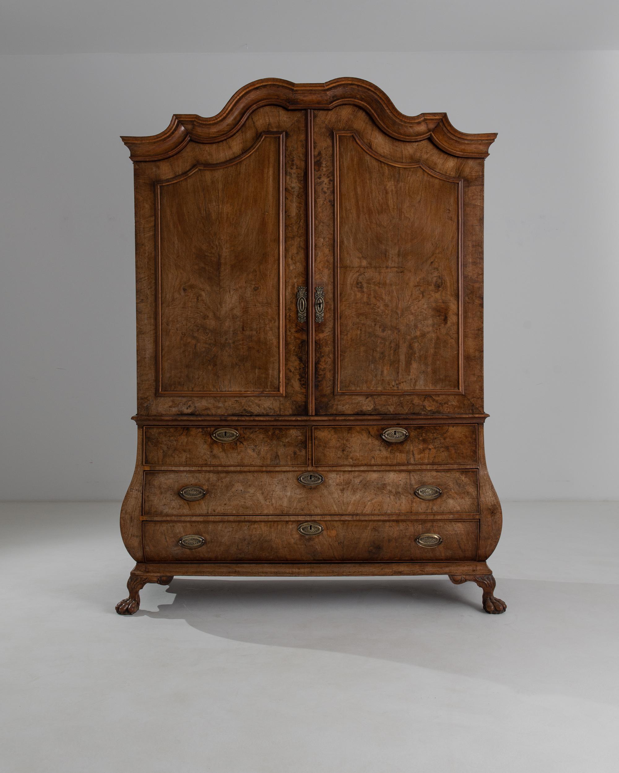 Built in the Netherlands circa 1800, the masterful construction of this antique wooden cabinet has lost none of its power to impress. The silhouette is bold yet sensuous: above, a sinuous molded cornice cascades in dramatic curves, while below a