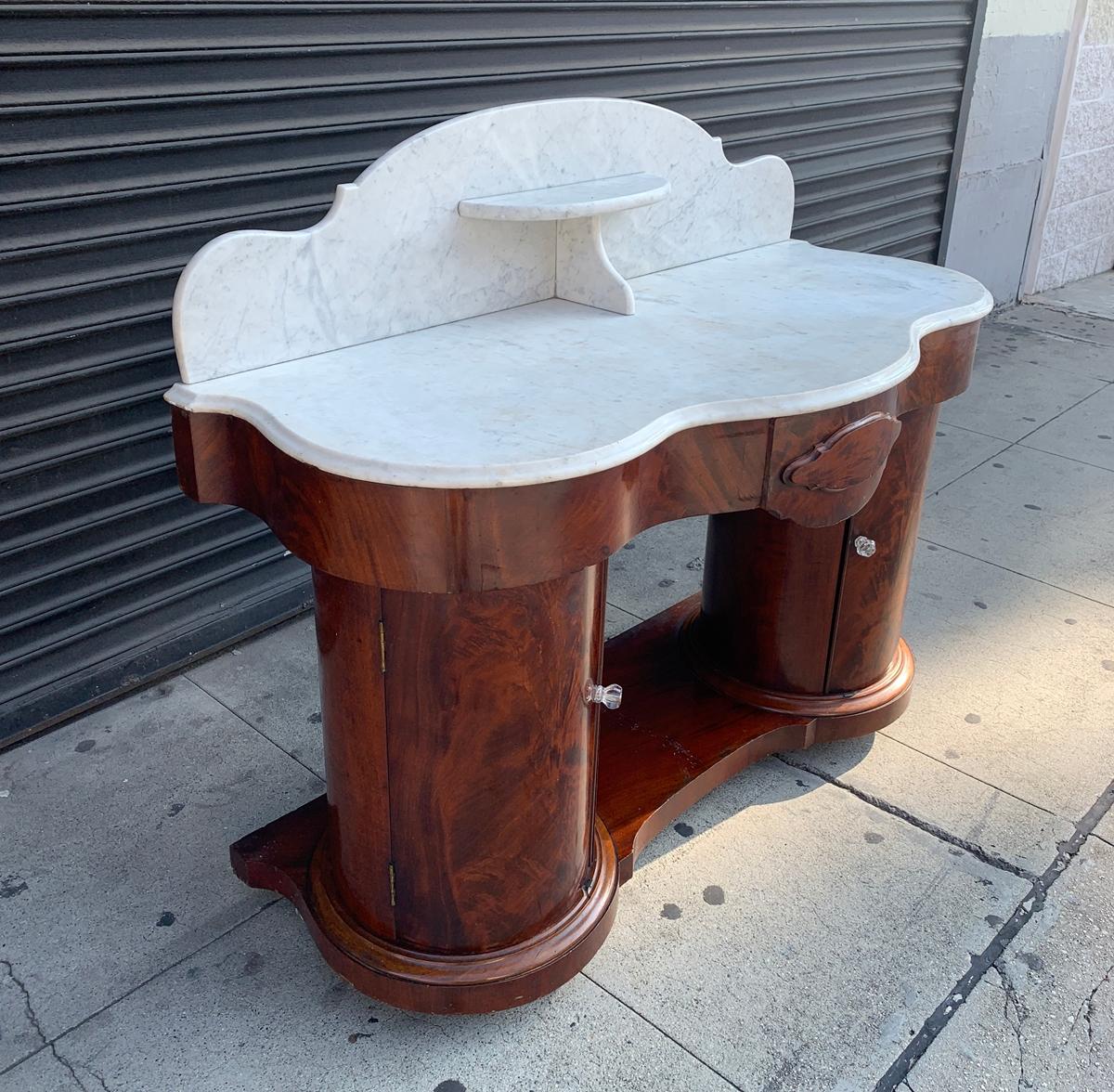 A magnificent antique Victorian entry table with marble top manufactured by F. Danby's of Leeds dating from the mid-late 1800s.

The piece is made in solid mahogany wood having a 2 round pedestals with one shelf on each pedestal and one middle