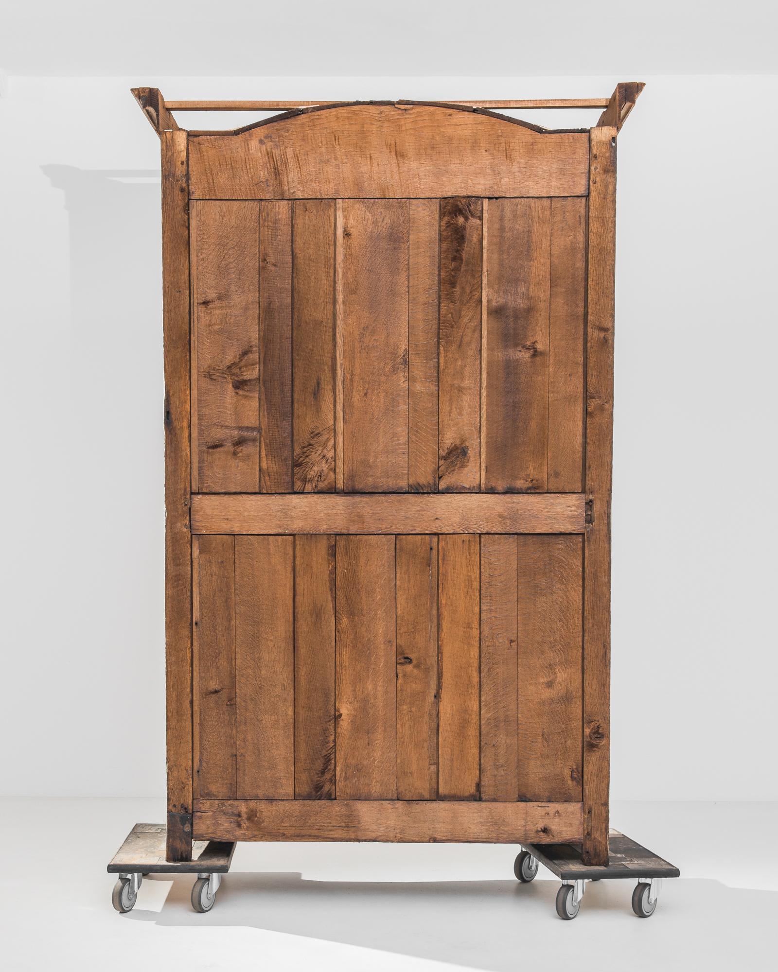 An oak armoire from France, circa 1800, with a majestic arched silhouette. The fluid peaks of the door panels mimic the curved crown of the cabinet, creating a sense of harmonious symmetry. The wood has been restored to a natural finish, revealing