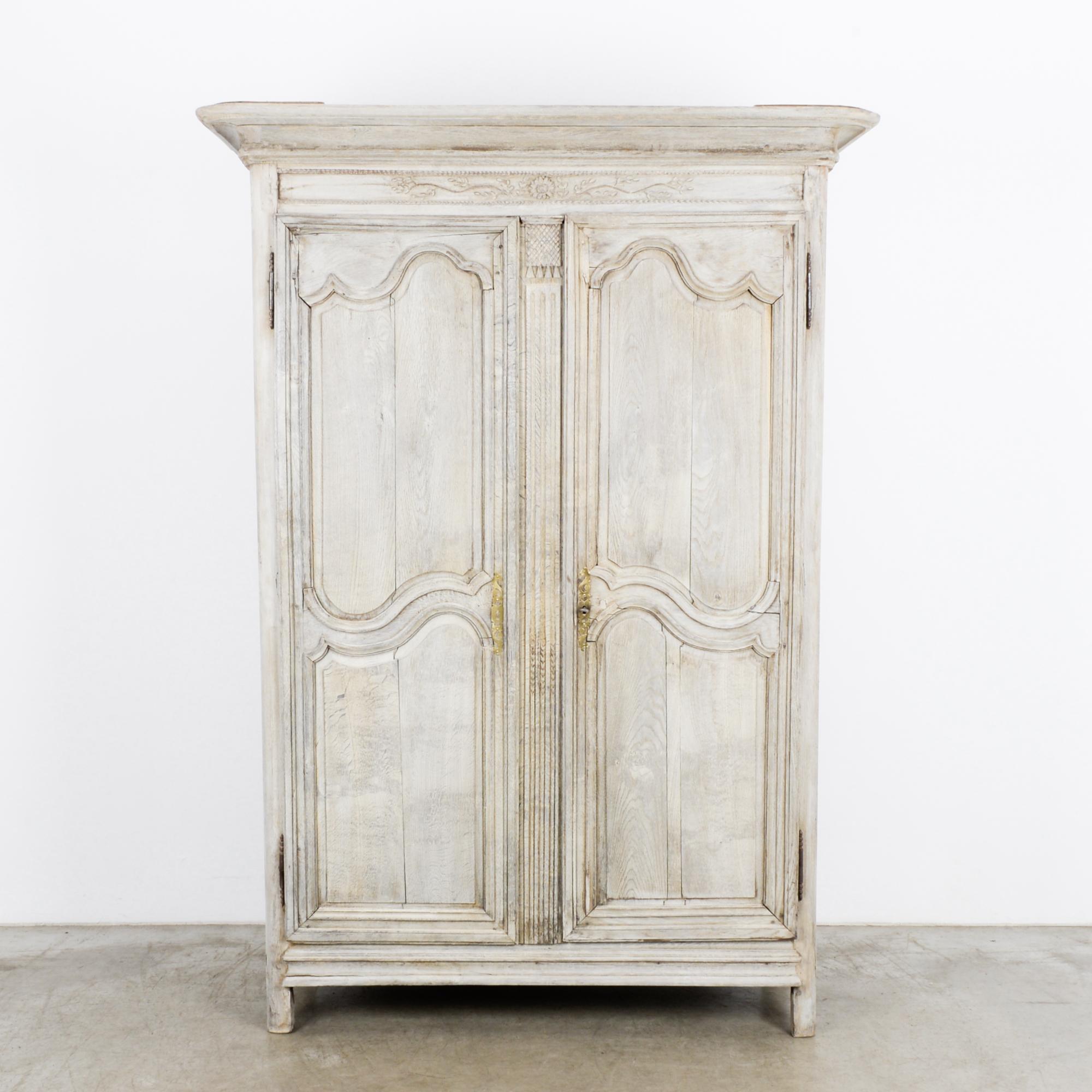 A bleached oak armoire from France, circa 1800. Paneled double doors with sinuous Baroque moldings open onto three shelves. The dark finish of the interior creates a dramatic contrast with the wood of the facade, restored to a clear, pearly white.