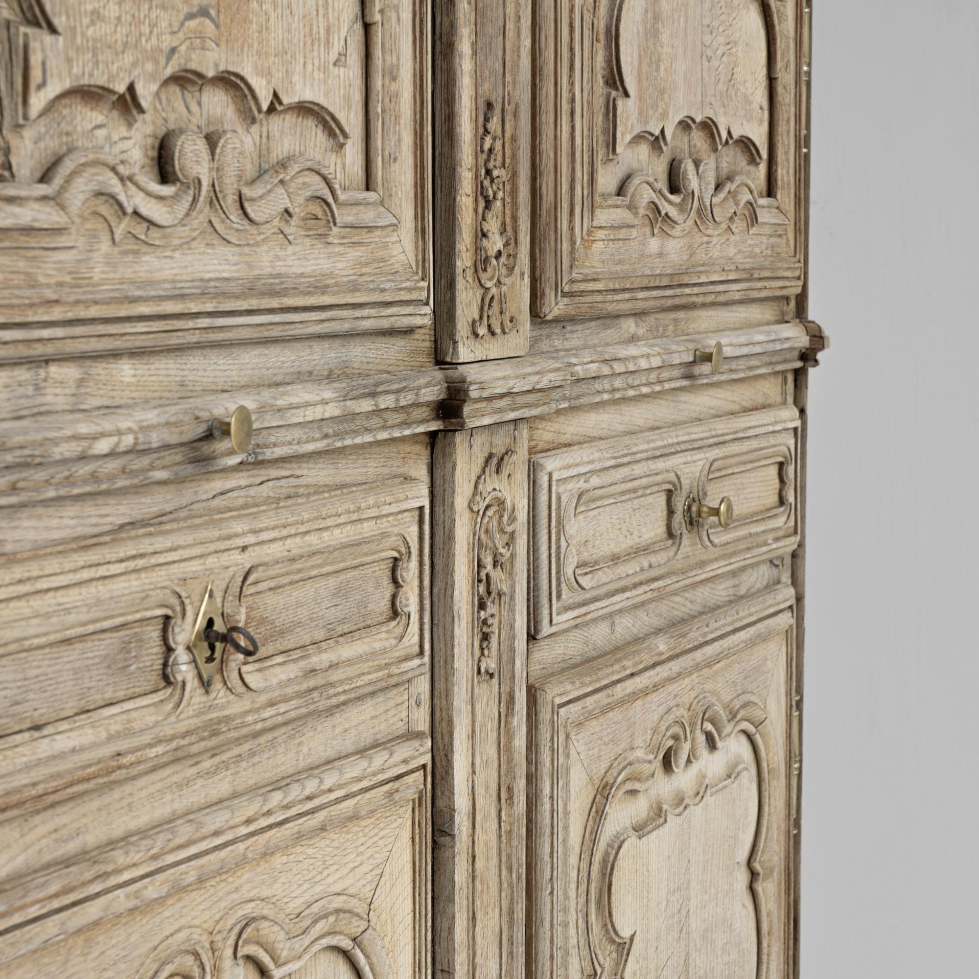 Dieser französische Kleiderschrank aus gebleichter Eiche aus den 1800er Jahren ist ein wahres Meisterwerk der Handwerkskunst und Raffinesse. Die Türen sind mit kunstvoll geschnitzten Details verziert, die eine atemberaubende optische Wirkung