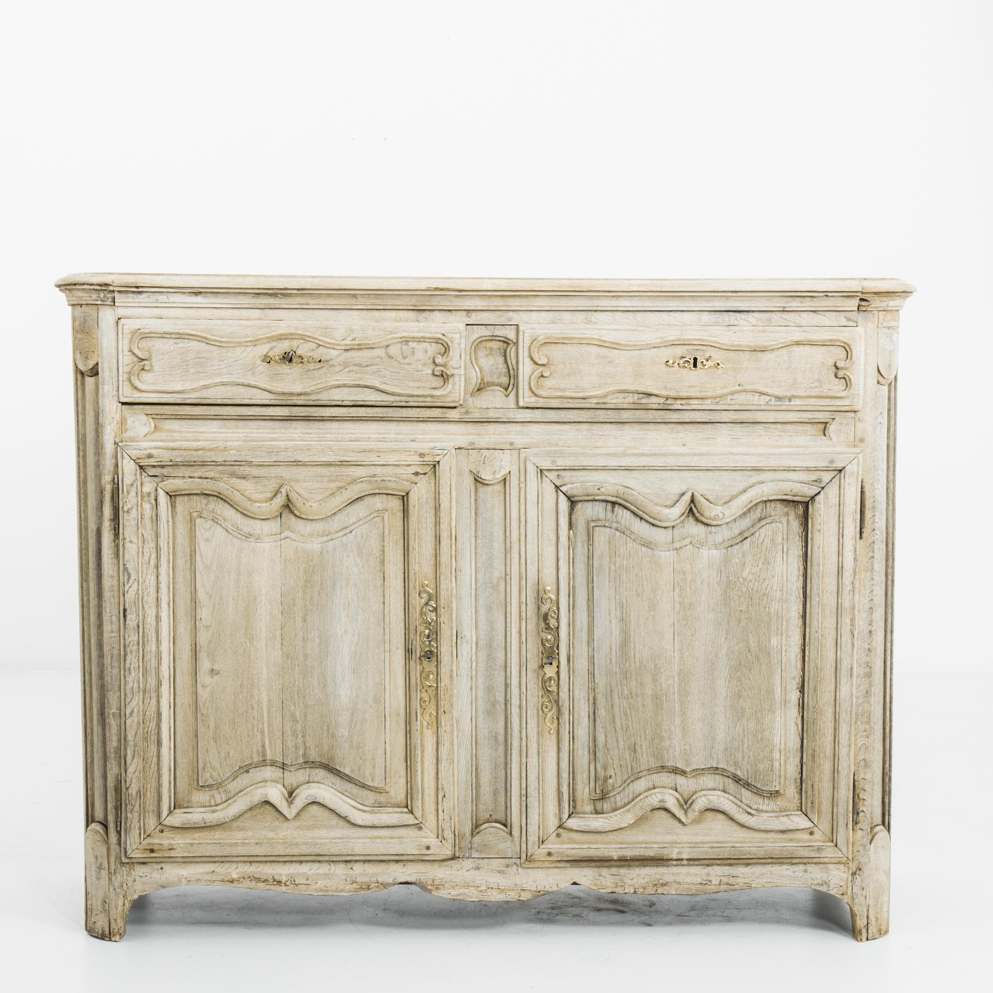 A two door and two drawewr oak buffet from 1800s France. The pale, pearlescent tone of the oak sets off the elaborate curves of the panelling to perfection. The contoured edges of the cabinet lend a graceful inflection to the silhouette; carved