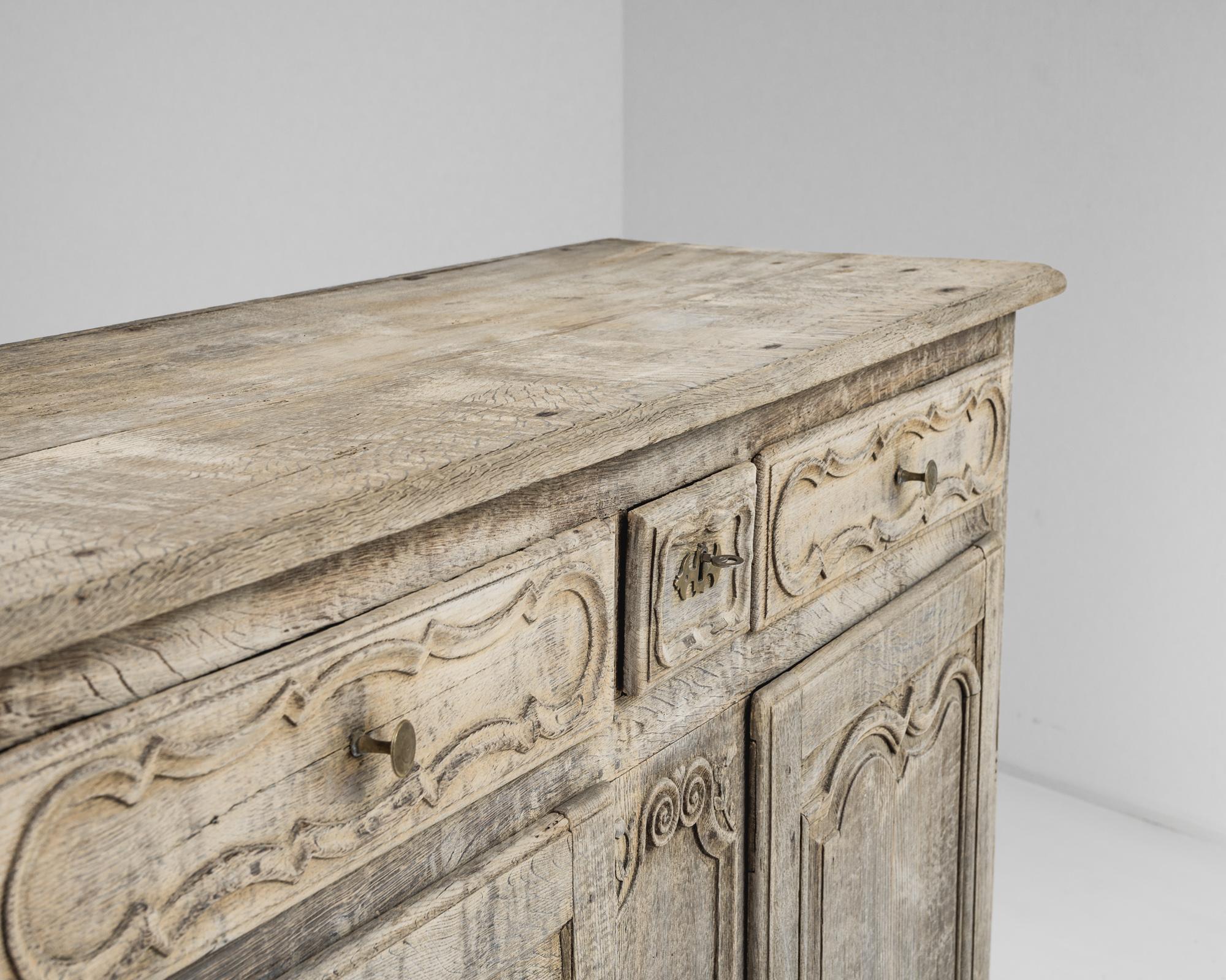 A bleached oak buffet from France, produced circa 1800. A simple buffet with a classic silhouette, this piece features an upper row of three drawers—two wider ones with brass knobs flanking a quarter width central one with key and brass