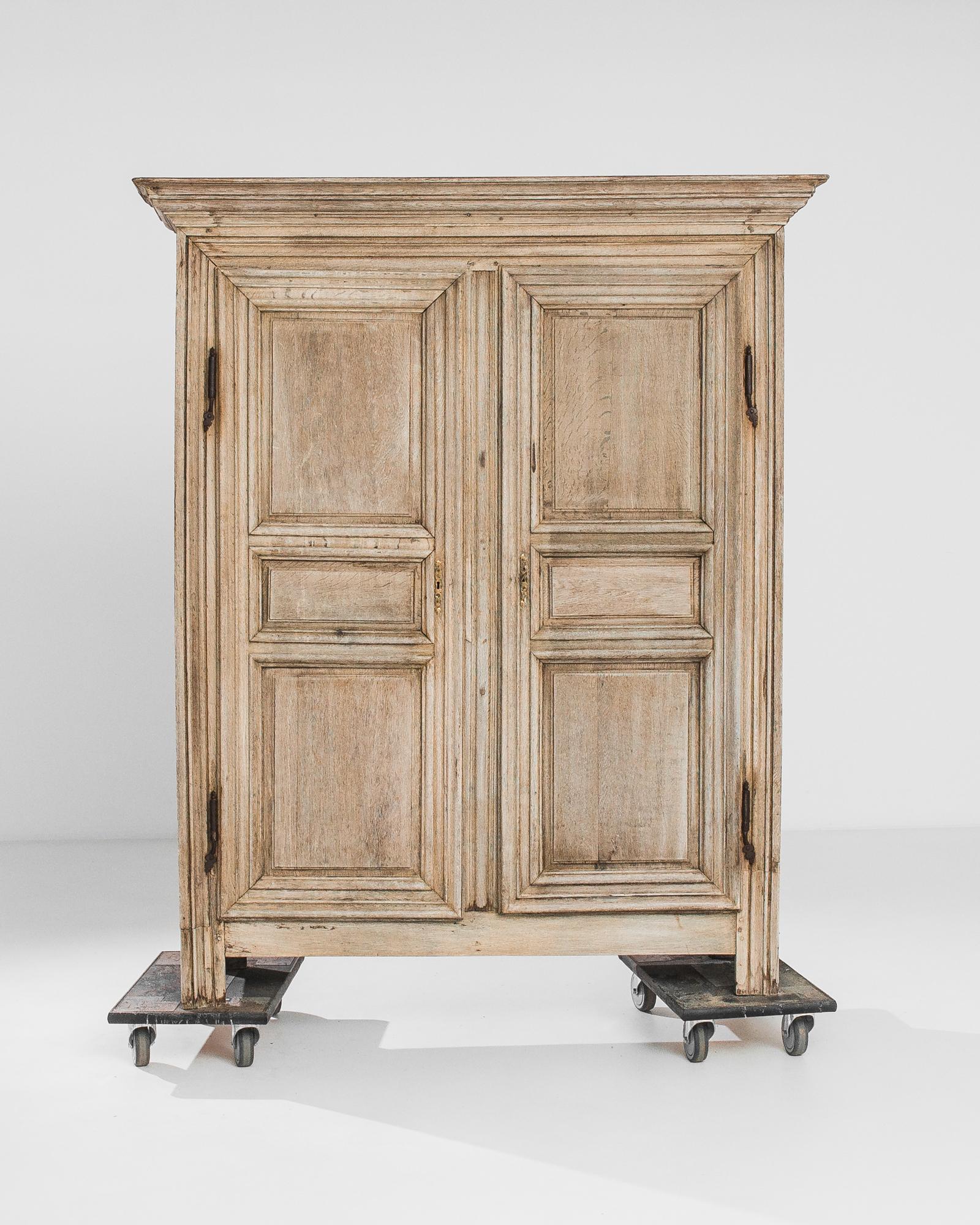 A bleached oak cabinet from France, produced circa 1800. An expertly crafted antique from the epoch that spawned the French empire, featuring a three shelf cabinet behind locking double doors. With a cornice like the wings of an omega, this stately