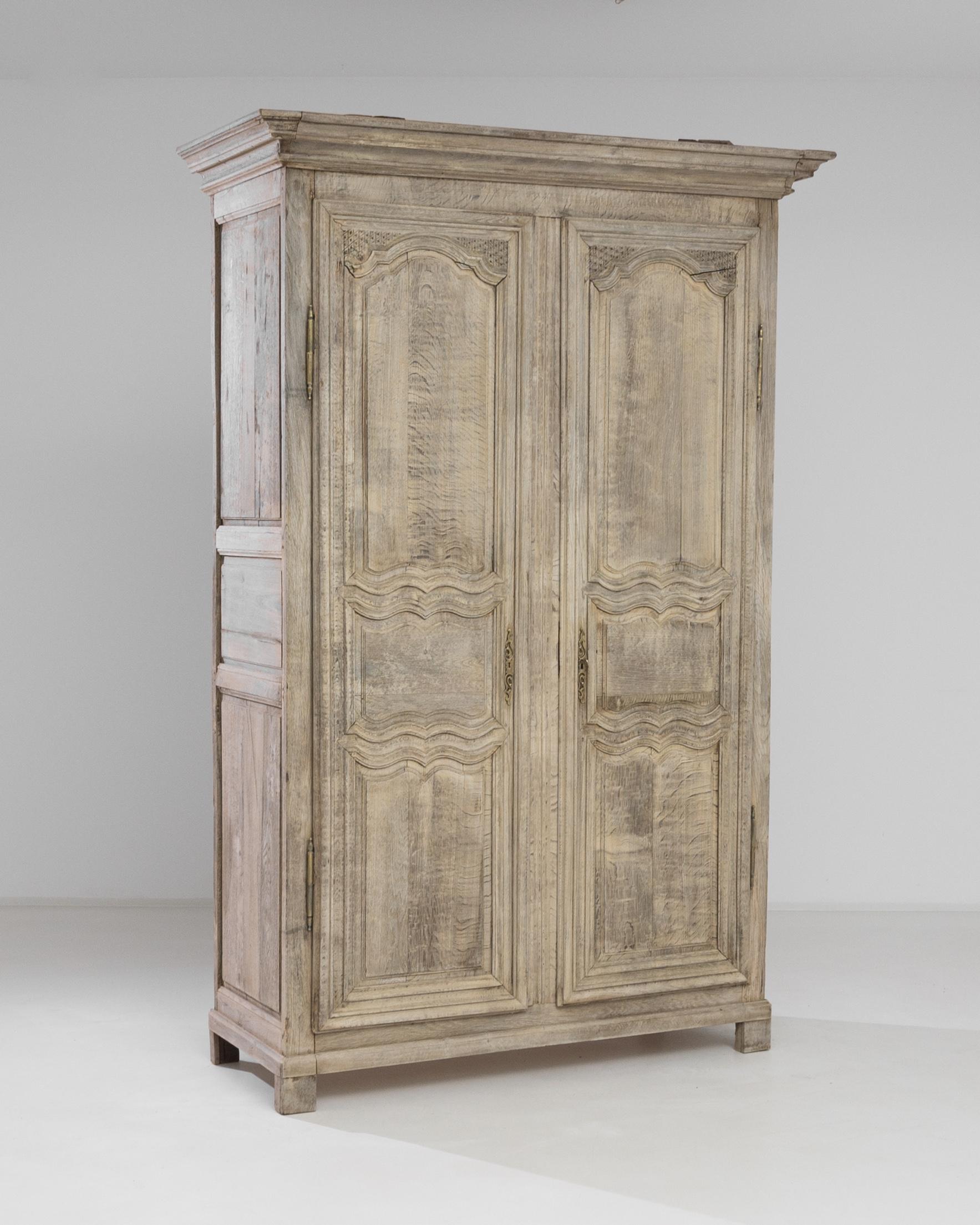 This tall armoire was crafted in France, circa 1800. Standing on bracket feet, this antique treasure features a molded cornice, gilded hardware and a carved case. The doors are ornamented with undulating beveled lines and discrete embossed fleurets