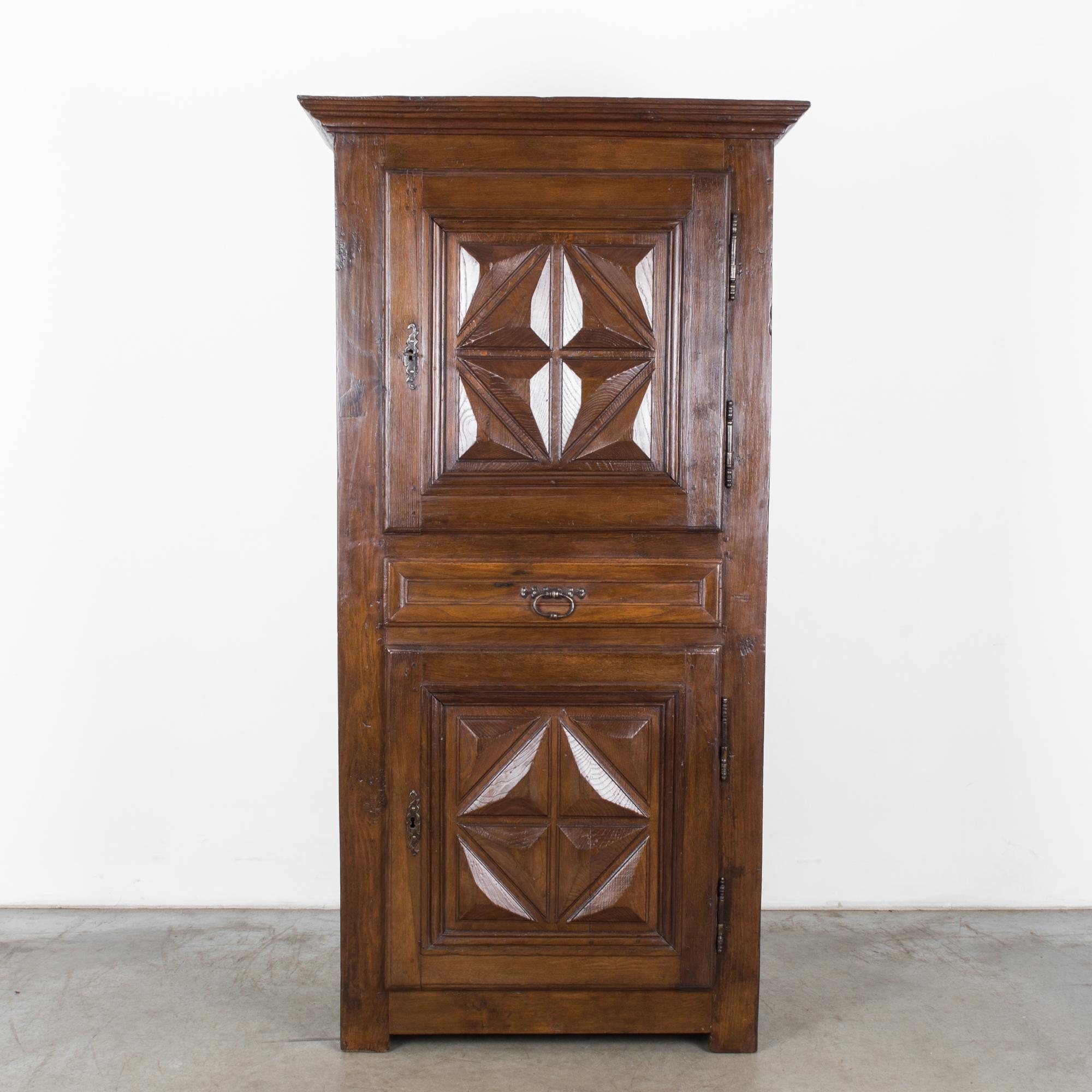 A tall wooden cabinet from France, circa 1880. An upper and a lower door are ornamented with a striking design of facetted raised panels. The jewel-like impression this creates is accentuated by the deep tone and rich polish of the wood. The doors