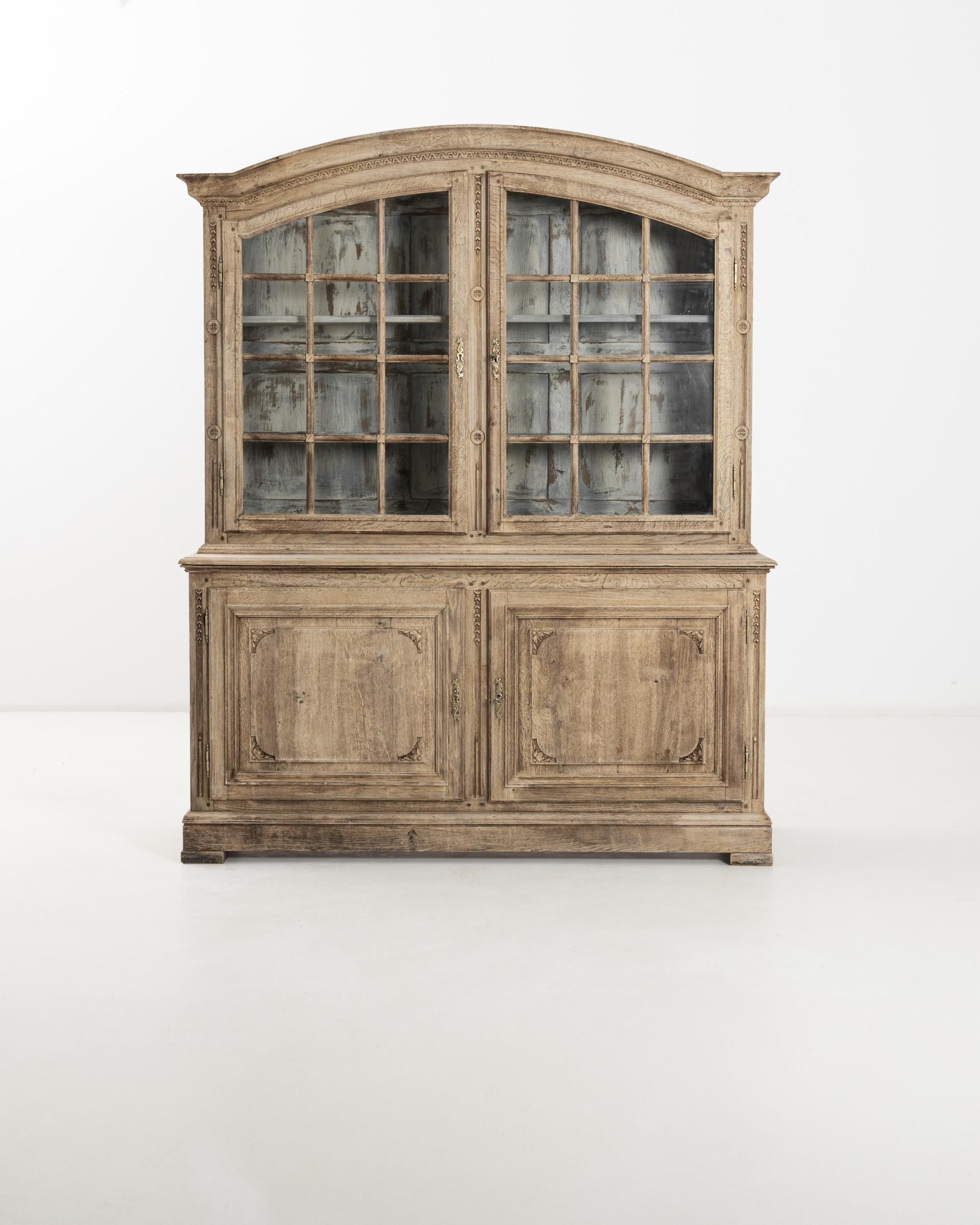 Carved details add glimmers of delight to this antique French Country vitrine. Made in Revolutionary France circa 1800, motifs of four-petalled flowers and languid garlands decorate the arched oak frame. Slender candles sporting tiny flames are