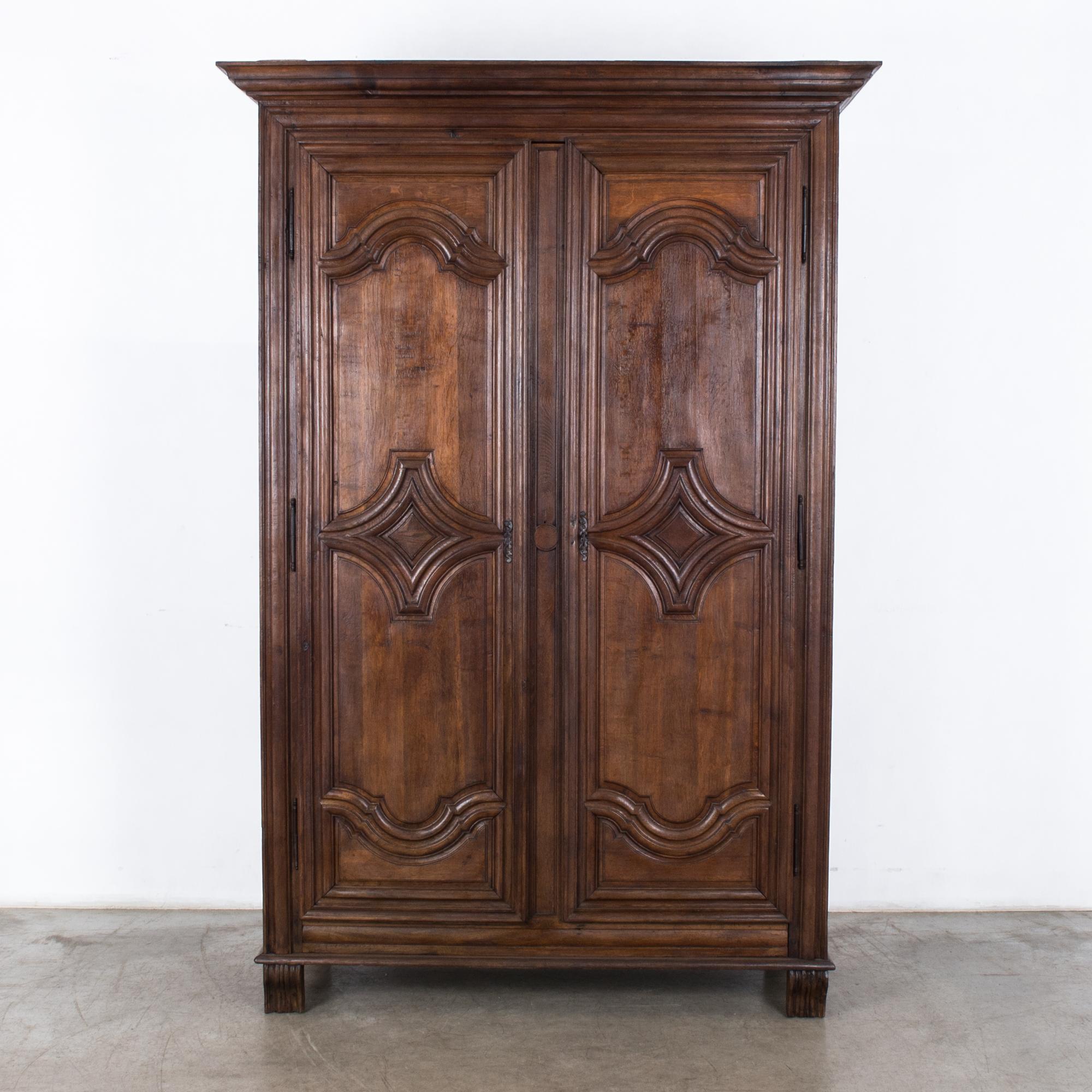 A wooden armoire from France, circa 1800. Tall in stature, with two doors that open onto a unique and practical interior arrangement: three interior shelves and a pair of pull out drawers with golden handles. The tone of the oak is warm and rosy,