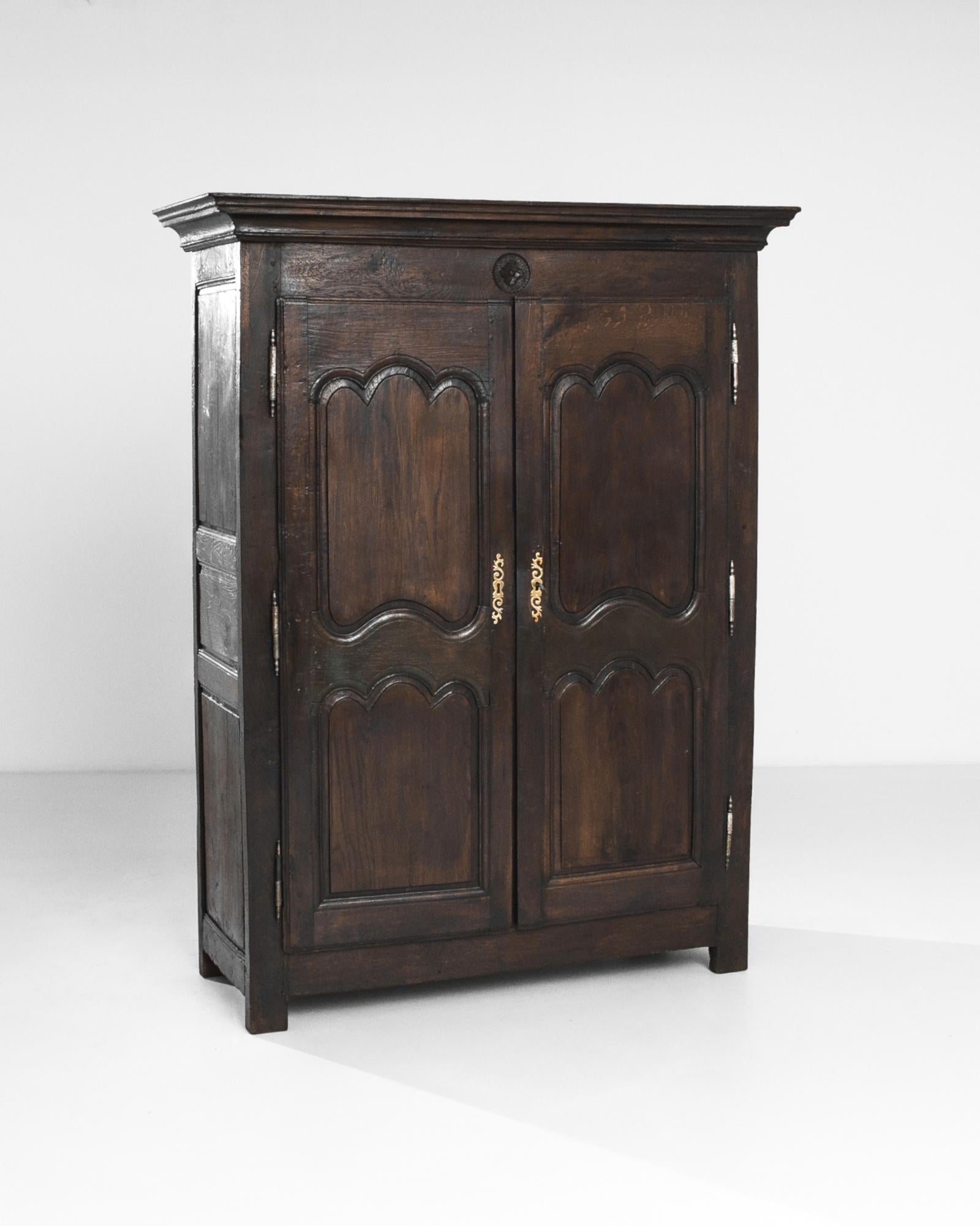 A wooden cabinet from France, circa 1800. Scalloped panels gift the cabinet a graceful symmetry, while the deep sable color of the wood, accentuated by a rich polish, lends a somber, enigmatic inflection. Broad double doors open onto a trio of
