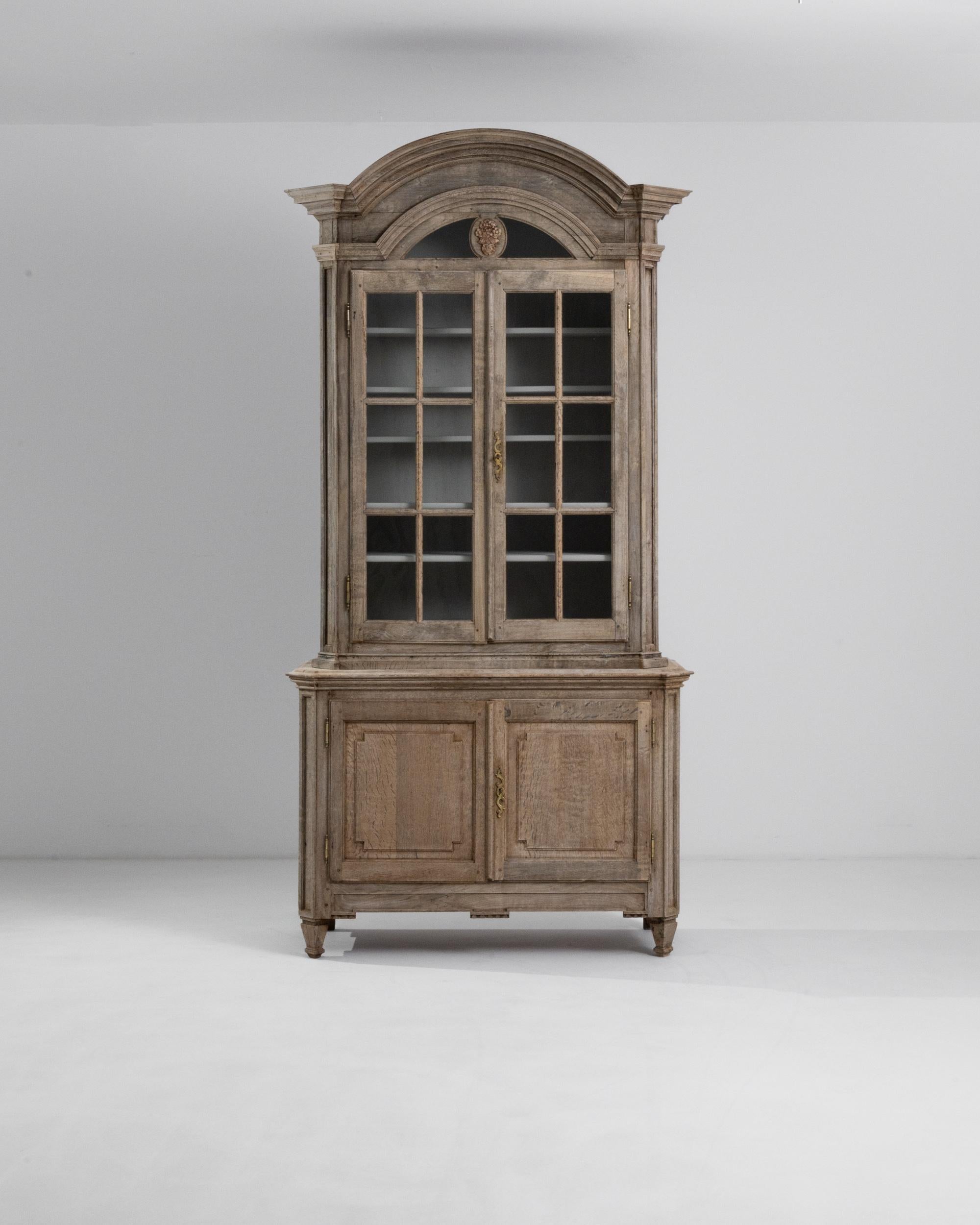 Neoclassical grandeur meets provincial charm in this antique oak vitrine. Made in France, circa 1800, the grand moldings of the arched cornice evoke the victorious architecture of the Napoleonic era —while mullioned windows below recall the houses