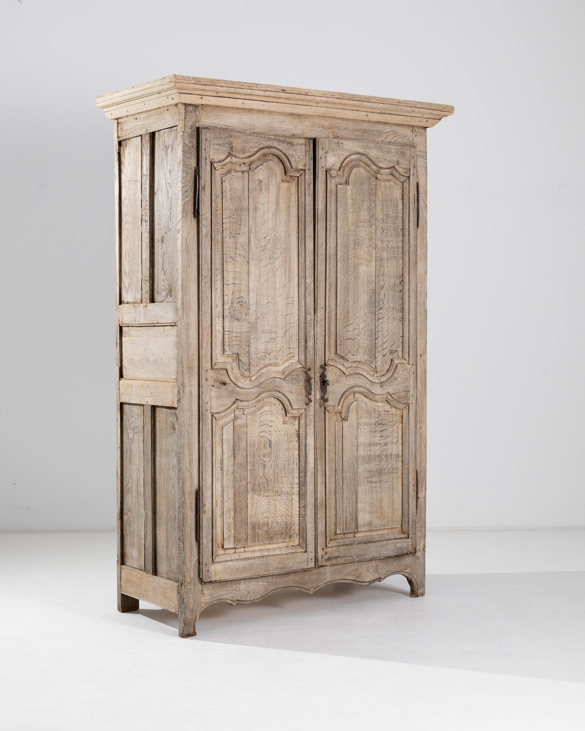 This antique wooden cabinet was produced in France, circa 1800. A tall cabinet standing on molded bracket feet and crowned by a cornice top, featuring an elegantly carved front and a scalloped apron. The wood has been carefully restored in our