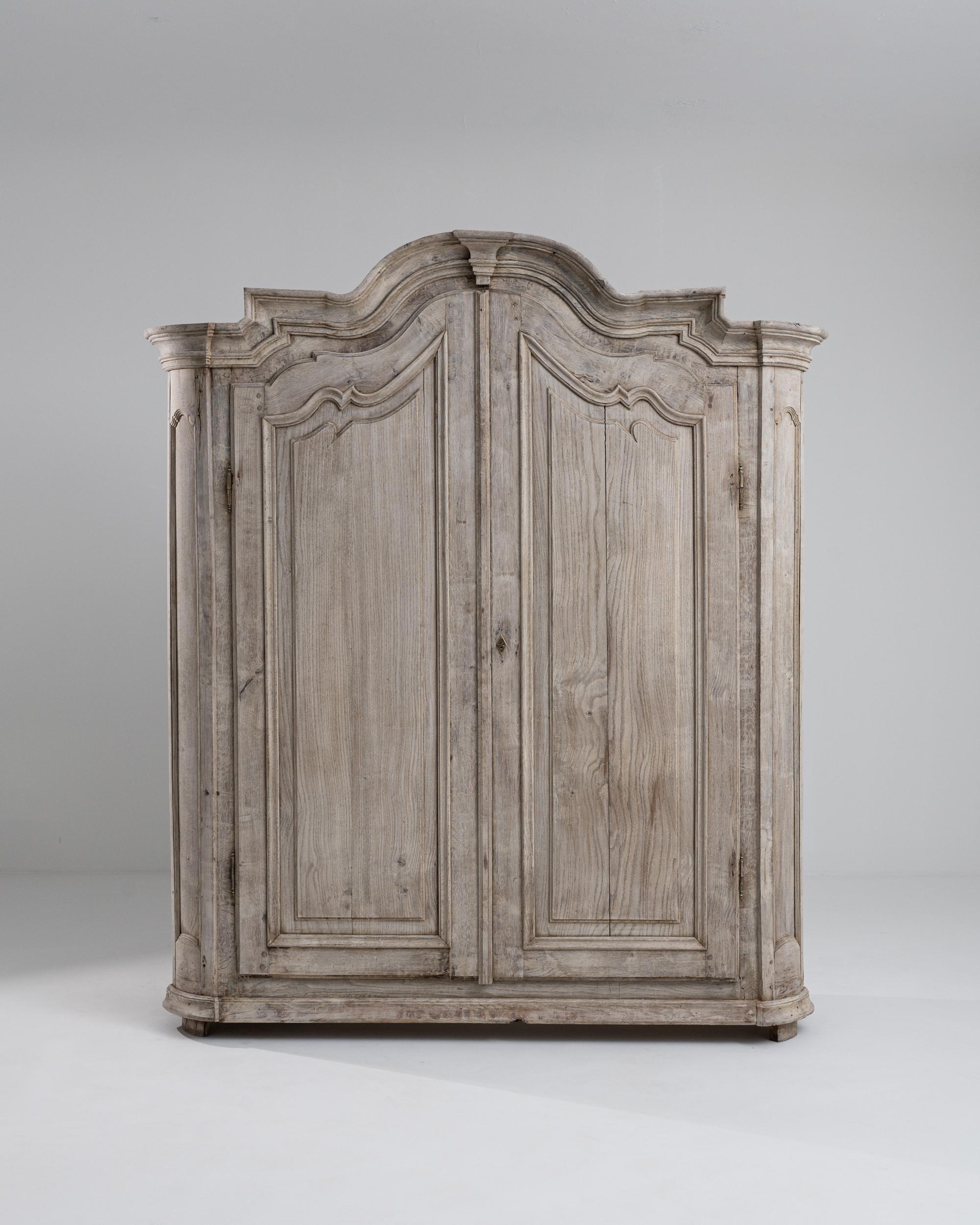 A wooden cabinet from 1800s France. This hulking wooden cabinet stands at seven feet high, its top molded edge carved into compelling angles and curves, almost like the roof of a gothic church. Oak construction has been painstakingly hand-chiseled,