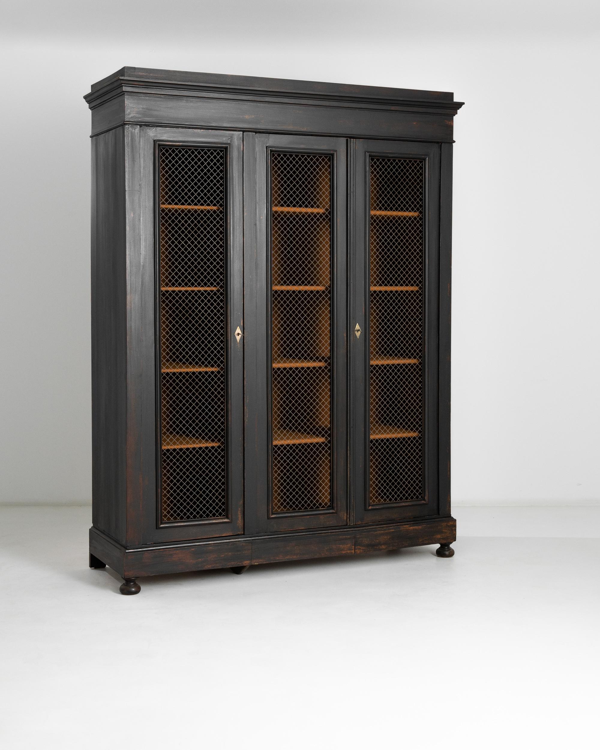 This antique linen cabinet was crafted in Germany, circa 1800. A beautifully patinated tall black cabinet standing on ball feet, featuring two front doors, an ample five shelves interior, three discreet lower drawers and a beveled top. The doors are