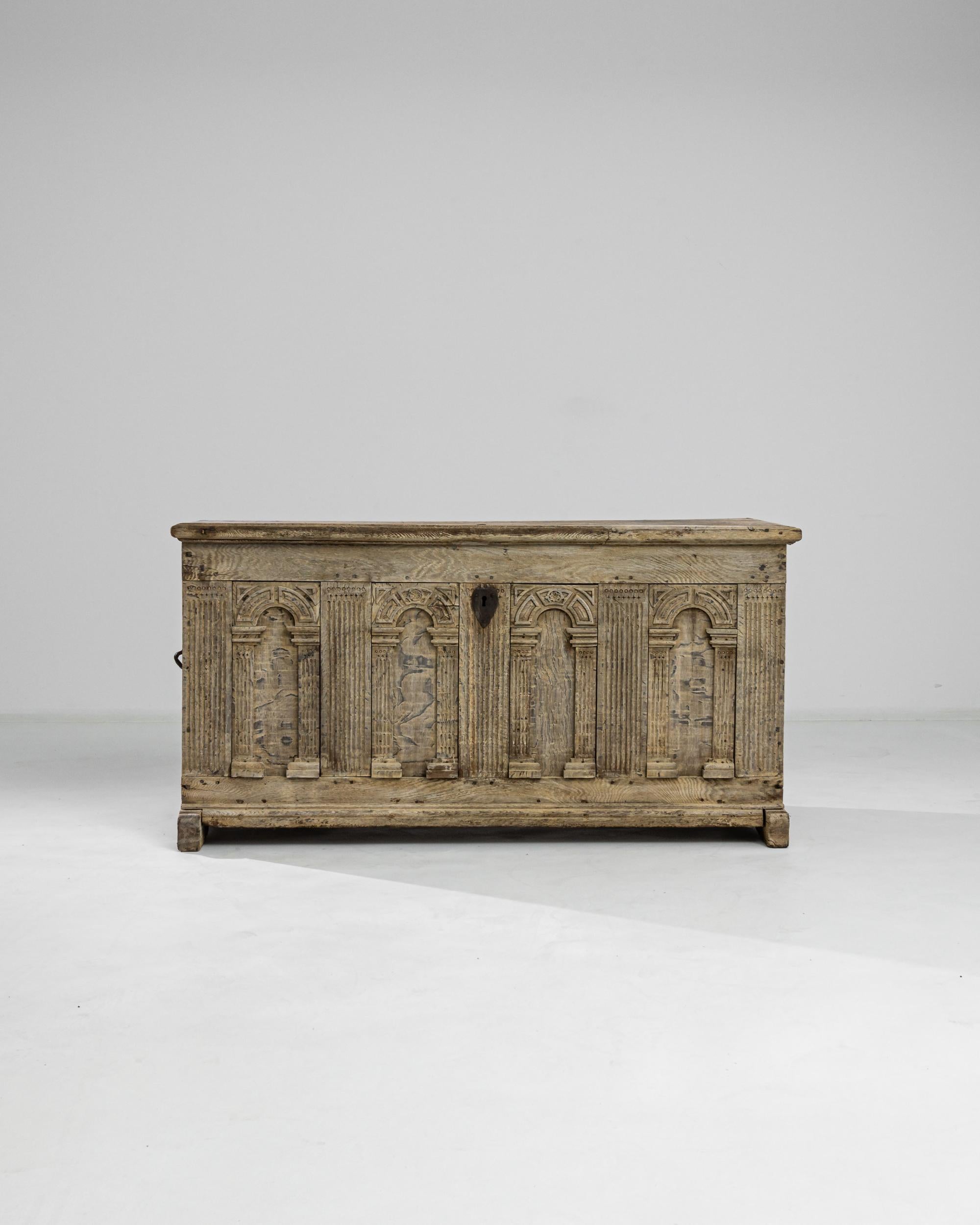 Ample and solid, this unique trunk was built out of oak in Germany circa 1800. The facade boasts four ornate panels hand-carved in the shape of classic arches, which are enlivened with ancient ornamental motifs. Original iron pulls on the sides