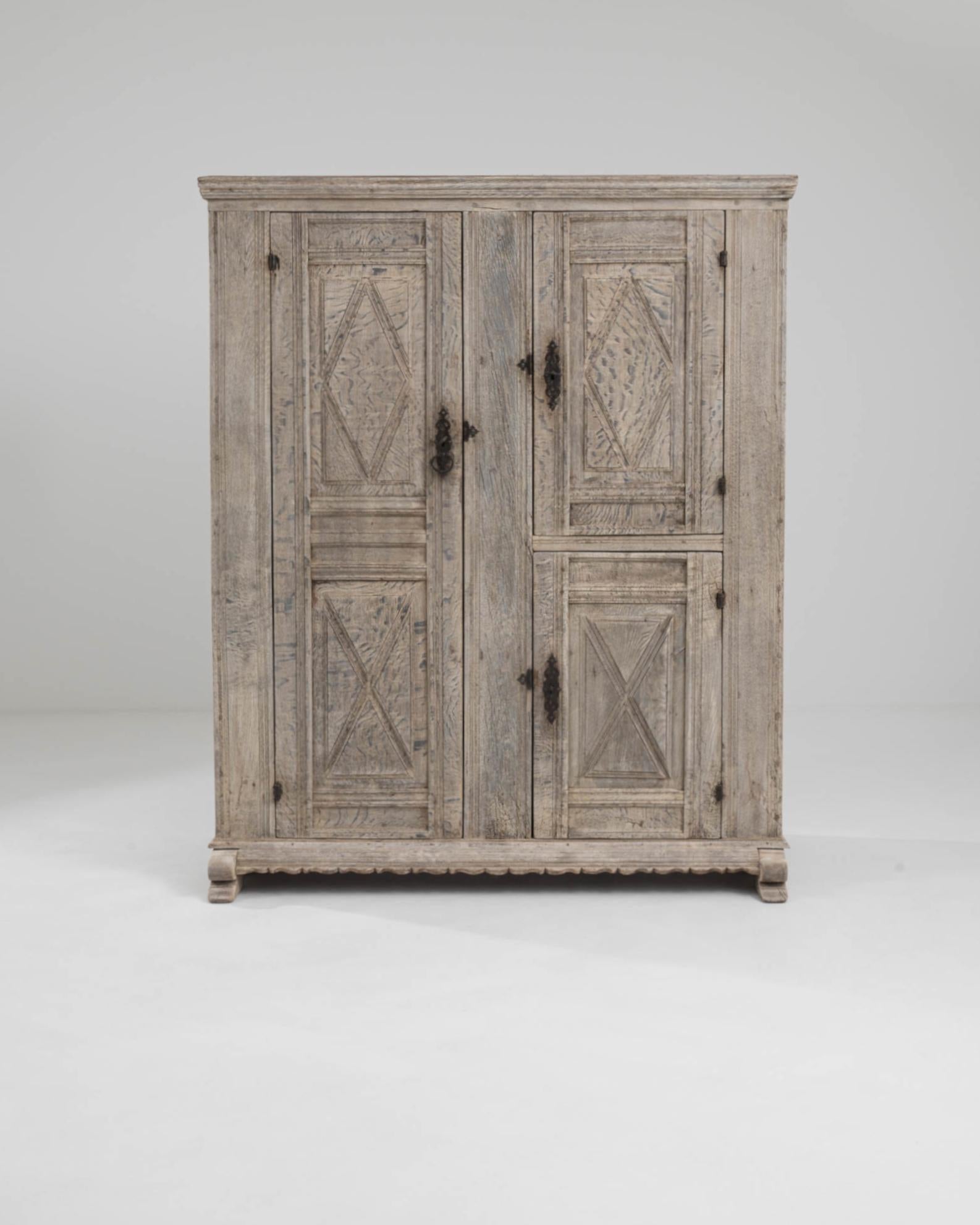 A wooden cabinet made in Germany circa 1800. Two lavishly sculpted doors, inscribed with diamonds and criss-crossing motifs, swing outwards to reveal two sets of asymmetrically positioned shelves. Ingeniously devised to store and protect the clothes