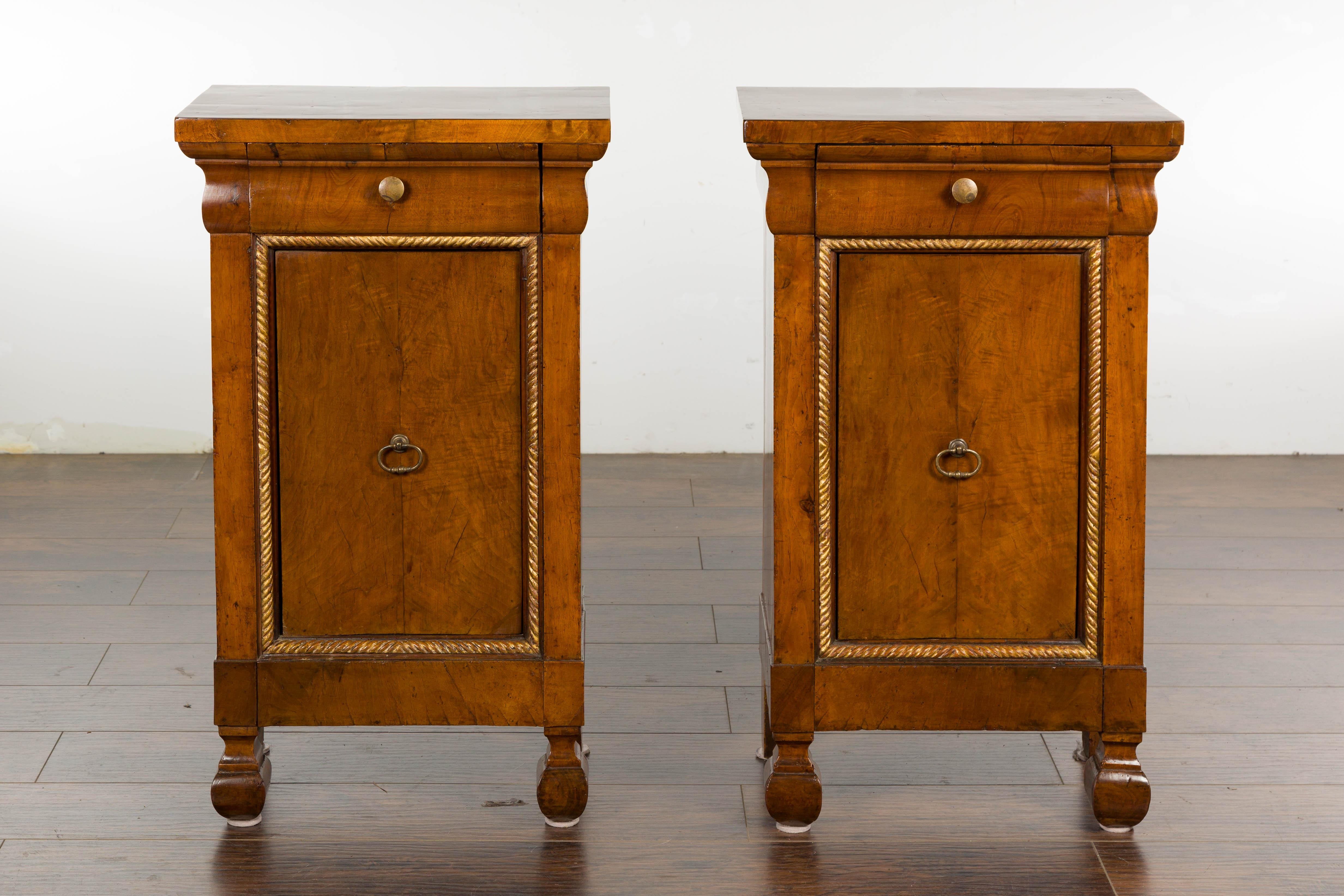 A pair of Italian walnut bedside cabinets from circa 1800 with single drawer and single door, carved giltwood twisted rope motif and carved feet. Discover an air of timeless elegance with this pair of 19th-century Italian walnut bedside cabinets, a