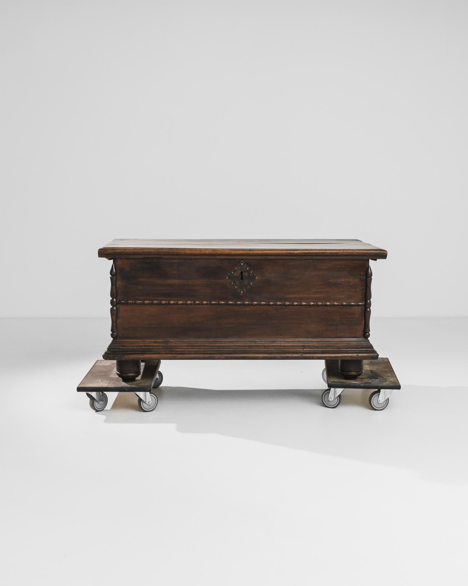 A wooden trunk from Southern Europe, produced circa 1800. A handsome antique trunk constructed of dark wood on four squat feet, featuring brass escutcheon and hinges and a flip-top lid. Rich details from the elaborate escutcheon to the woodwork