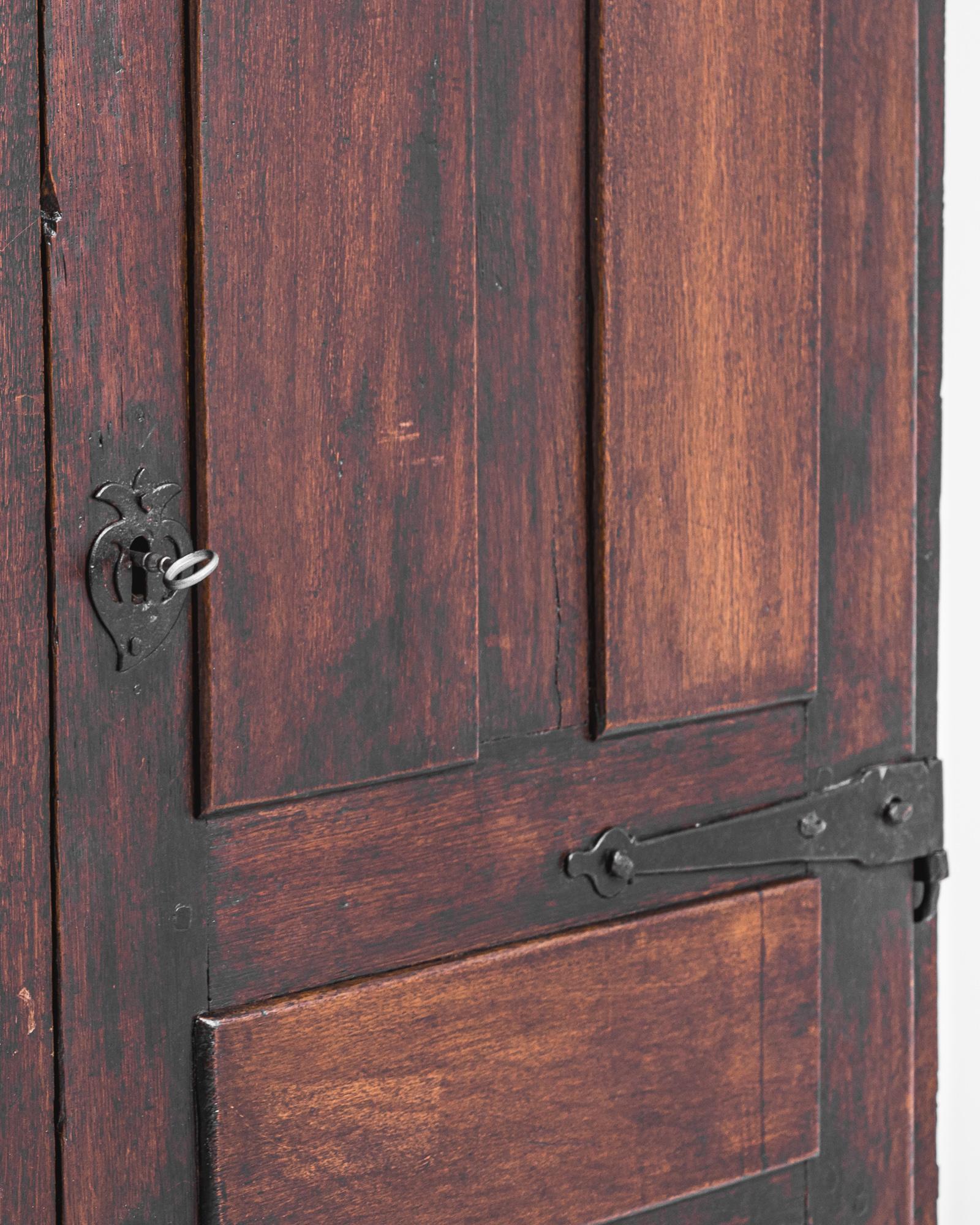 A wooden cabinet from Spain, produced circa 1800. At a height of six and a half feet, this antique features a double door upper cabinet hanging from heavy iron hinges and two sliding drawers with dangling pulls, all coated in a dark stain that gives