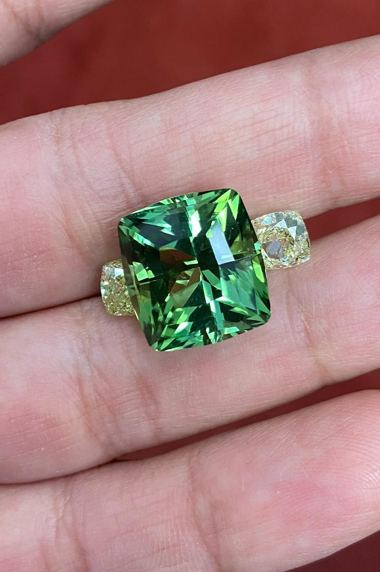 An impressive 18.02-carat GIA certified, untreated minty-green Tourmaline from Congo is flanked by two untreated GIA certified, fancy yellow diamonds totaling 3 carats, designed in platinum with 18K yellow gold. 