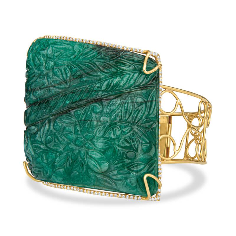 A one of a kind bracelet featuring a 180.87 carat carved natural emerald surrounded by .79ctw of 58 round diamonds and a scrolling design at the bangle. The asymmetrical emerald curves to fit the wrist beautifully. Set in 18 karat yellow gold with a