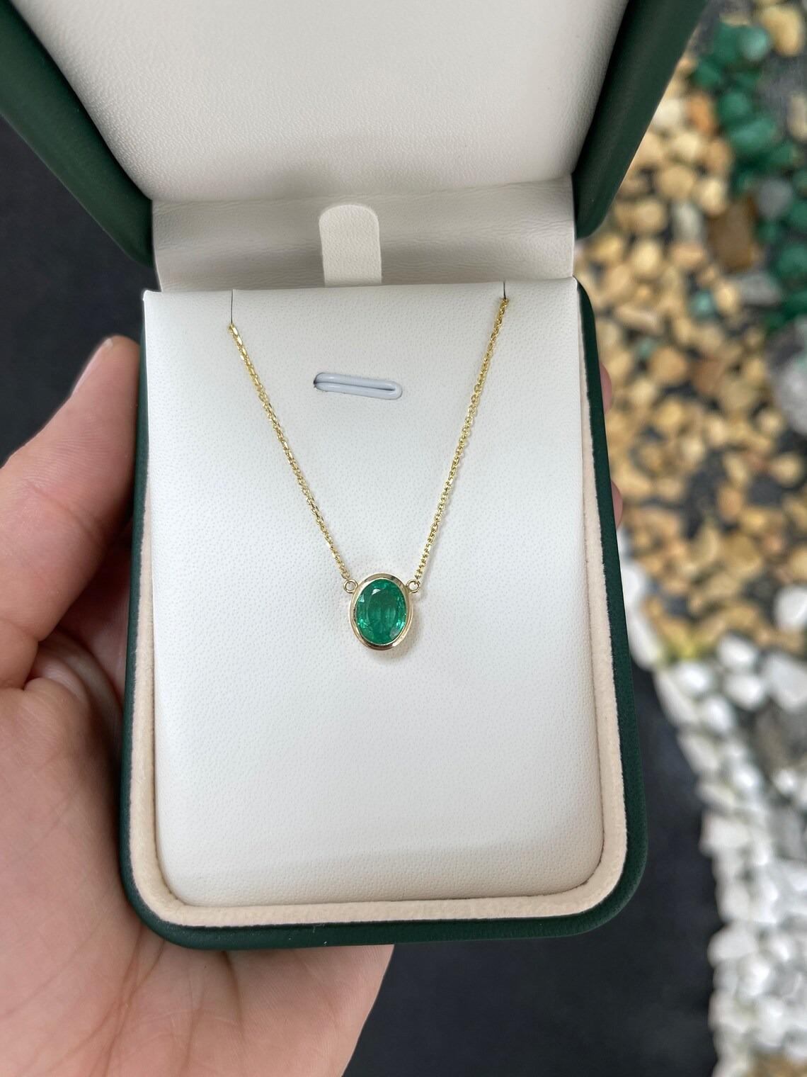 This stunning emerald necklace features a beautiful oval-cut emerald with a vivid medium green hue. The emerald is securely bezel set in a 14k gold solitaire pendant that measures 18 inches in length. The pendant is attached to a thin cable chain,