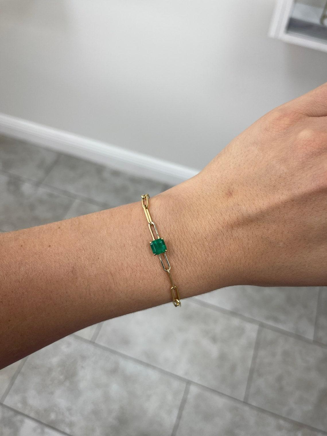 Introducing an exquisite emerald paperclip bracelet that exudes timeless elegance. At its center sits a stunning 1.80-carat asscher cut emerald, radiating a deep green hue with semi-transparent clarity and captivating luster. The emerald is