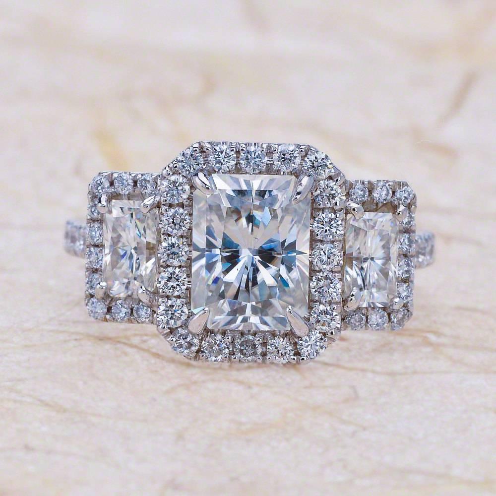- Center Stone: Radiant Cut Moissanite 8x6mm (1.80ct)
- Radiant Cut Side Stones: 5x3mm (0.30ct each)
- Side Stones: Round Cut Diamonds 0.50ctw / Graded G SI1
- Metal: 14K White Gold

This piece is made-to-order. Please allow up to 7 Business Days to