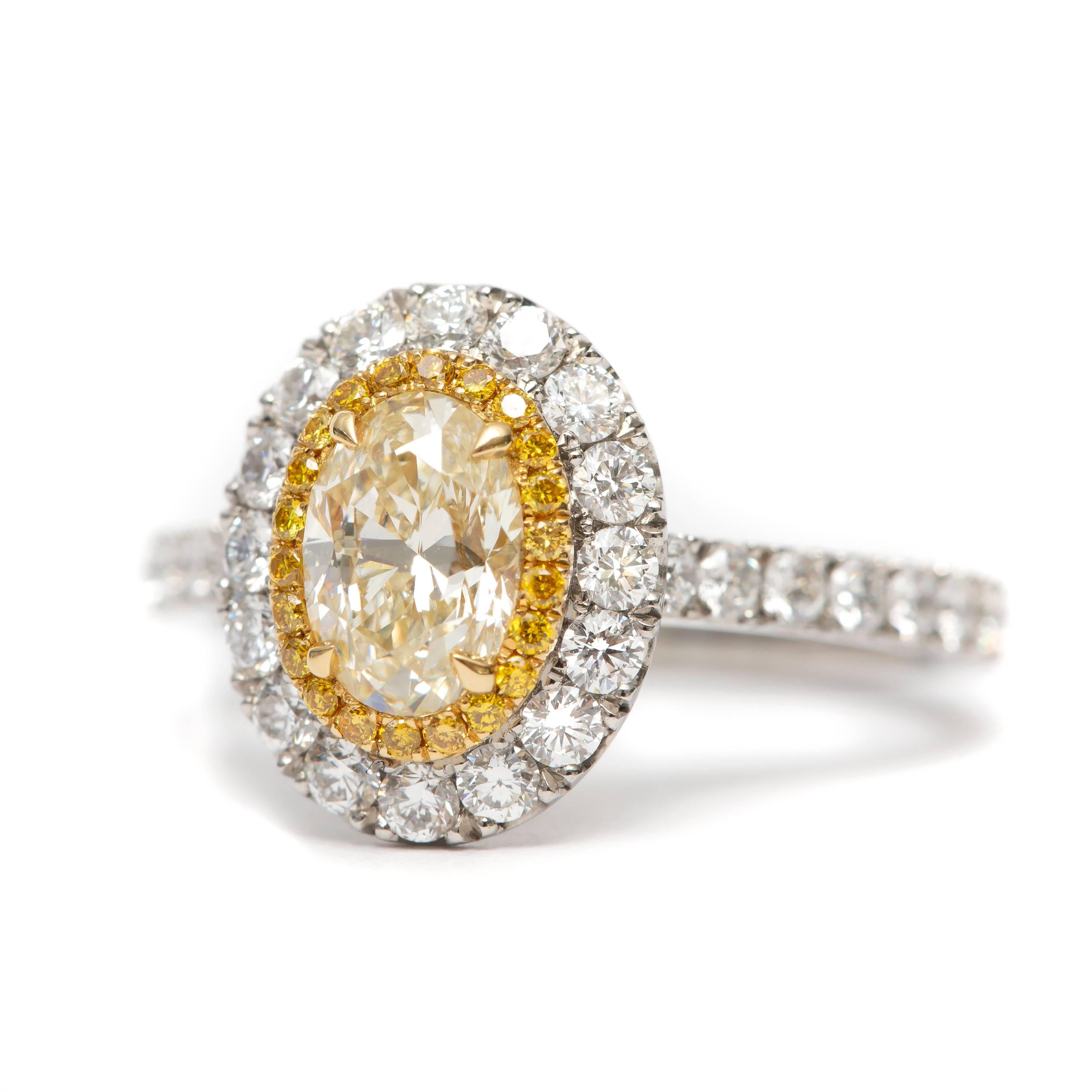 This spectacular 0.90 Carat Oval Brilliant Diamond Fancy Light Yellow which is set in the center with 0.11 Carat of Round Brilliant cut Fancy Intense Yellow Diamonds on the perimeter, with 0.80 Carat White Color G/H Clarity SI1 of Round Brilliant