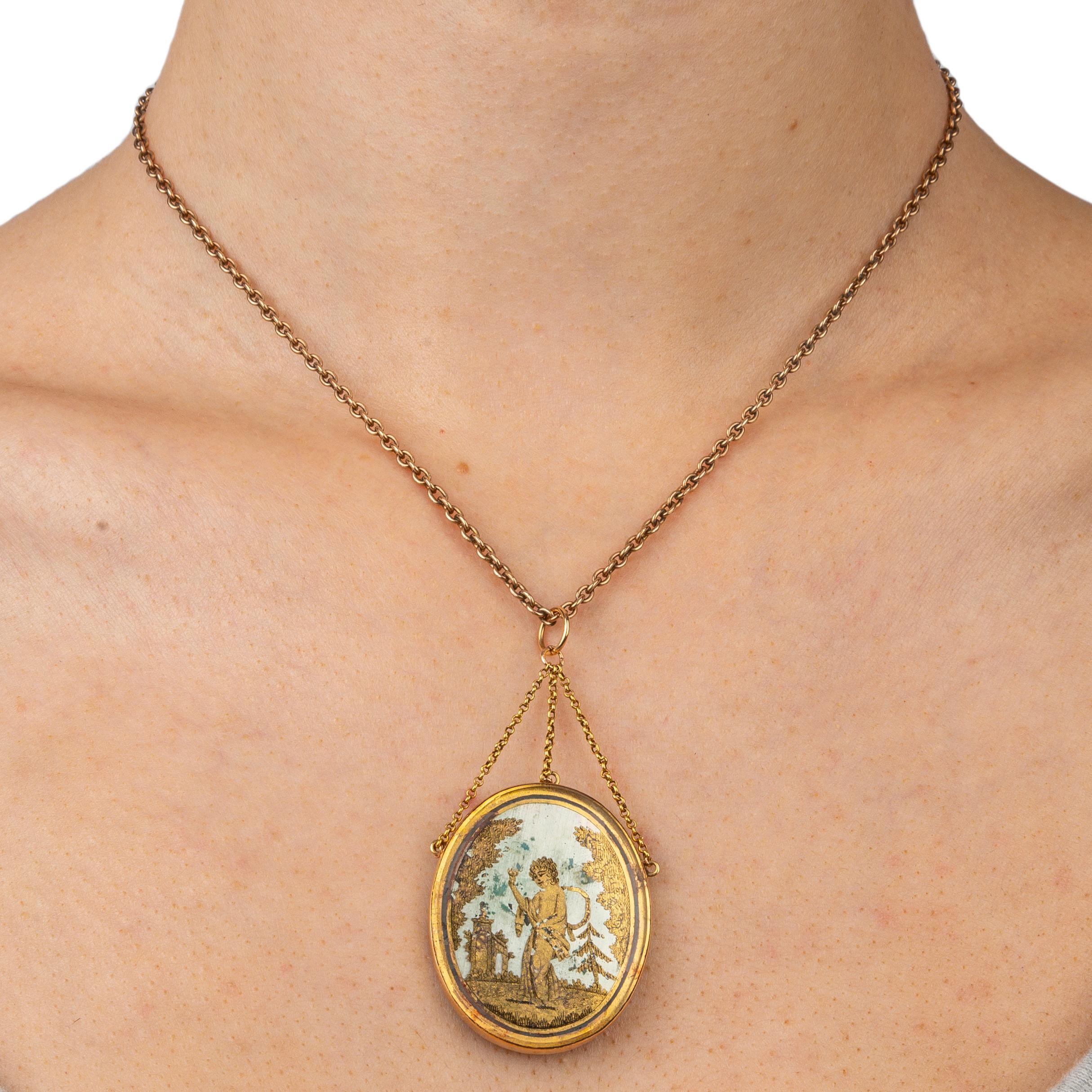 A beautiful and rare French pendant from the Napoleonic era, of etched gold leaf on glass depicting the figure of Eros holding a torch in a wooded landscape, the frame attached to three small gold chains joined by a central ring, mounted in 18k