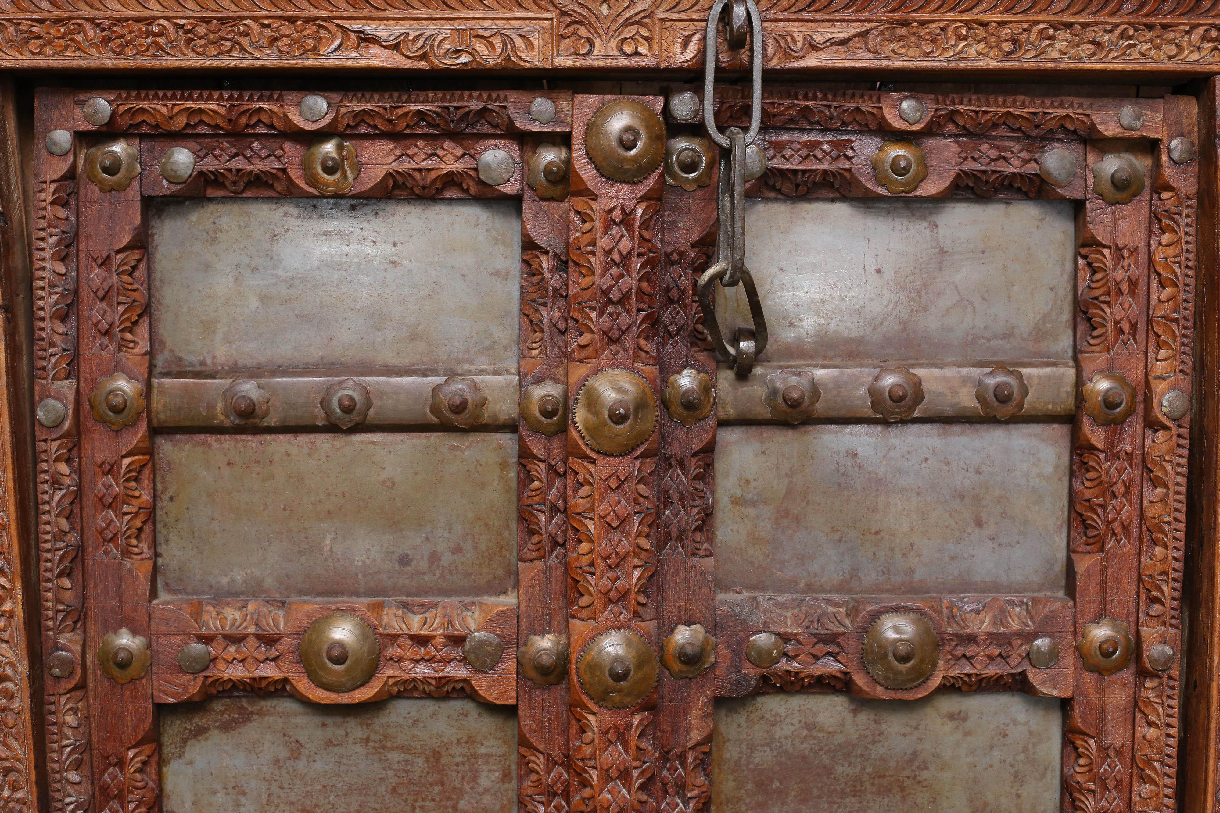 An extremely rare 200 years old highly ornamental teak wood door from a farm house in Western India. The door is heavily reinforced with metal sheets and hand-forged iron studs. The doors revolve around one peg on the top and one in the bottom. Old