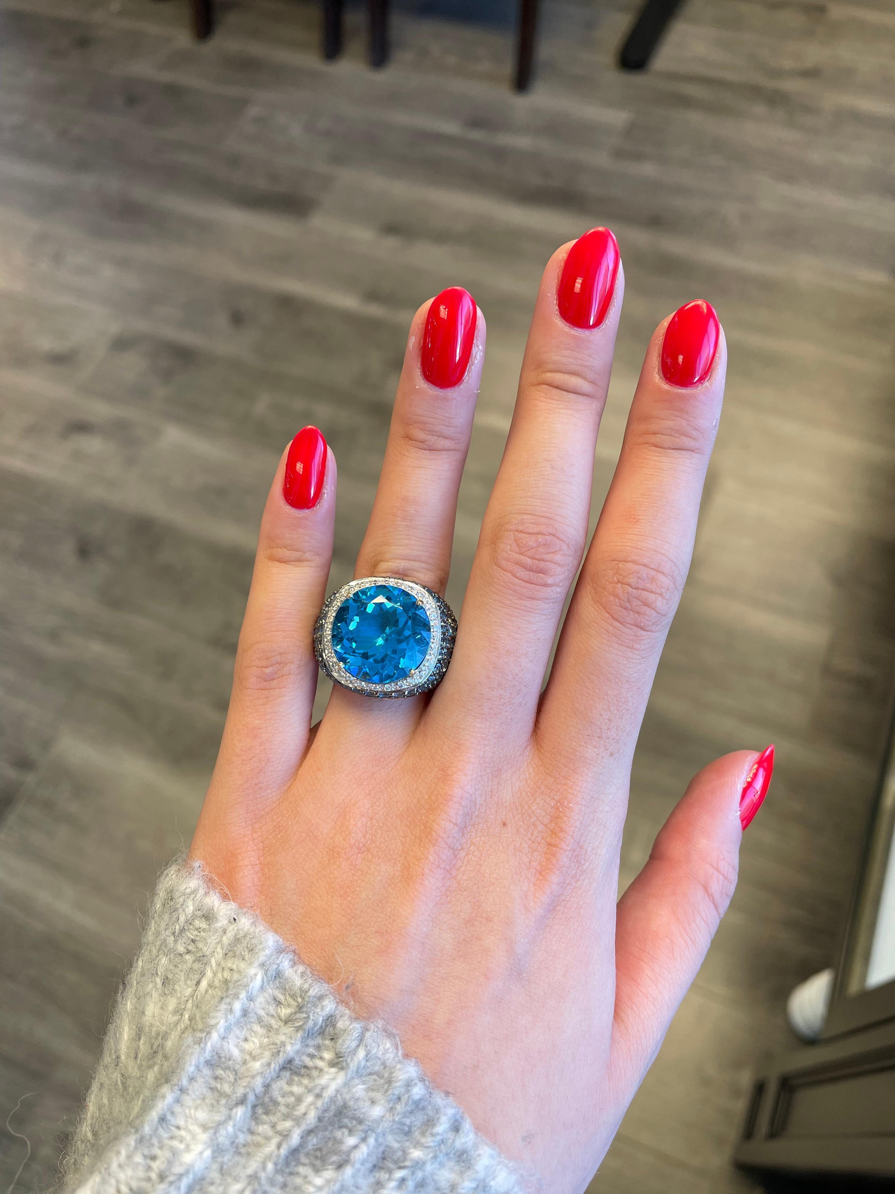 Exquisiter und lebendiger Blautopasring. 
Zentraler Blautopas von 18,13 Karat, ergänzt durch weitere 3,40 Karat Petit Topas und 0,35 Karat runde Brillanten. 21.88ct Gesamtgewicht der Edelsteine, gefasst in 18 Karat Weißgold mit schwarzem Rhodium.