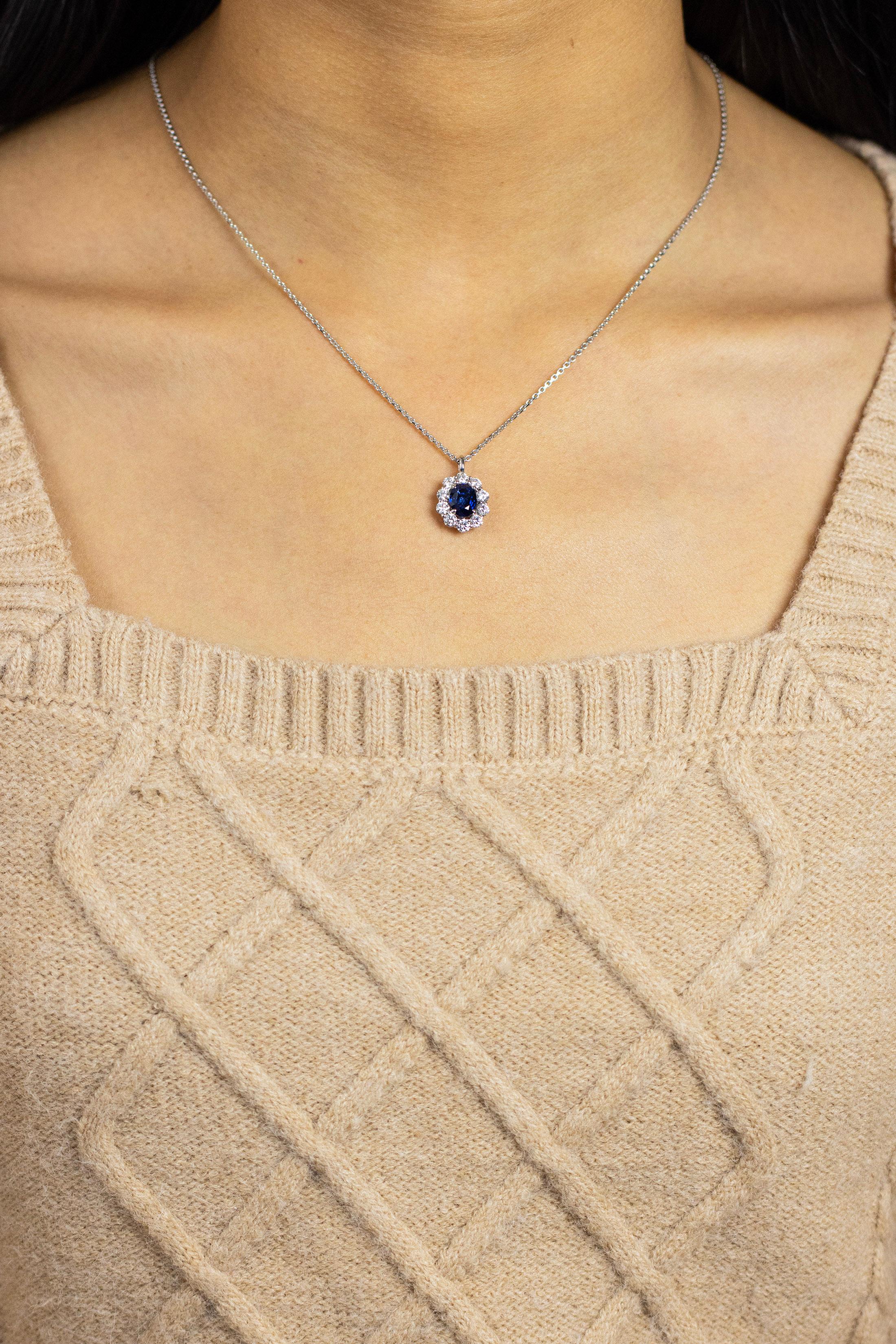 A classy pendant necklace showcasing an oval cut color-rich blue sapphire weighing 1.82 carats, set in a classic four prong basket setting. Surrounded by a single row of round brilliant diamonds weighing 1.06 carats total, set in a shared prong